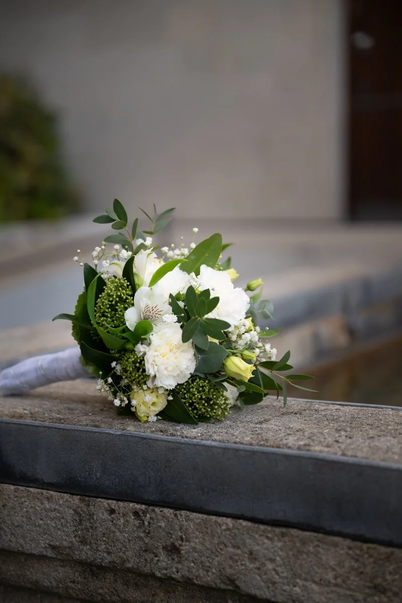 Ein Brautstrauß mit weißen Blumen und grünen Blättern auf einem Stein.