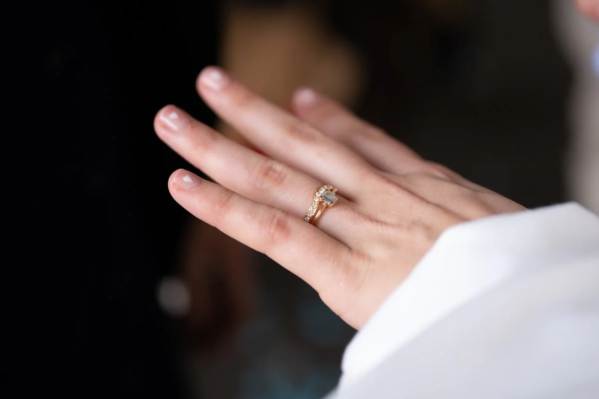 Nahaufnahme einer Hand mit einem Ehering und einem Verlobungsring am Finger, getragen auf einem schwarzen Hintergrund