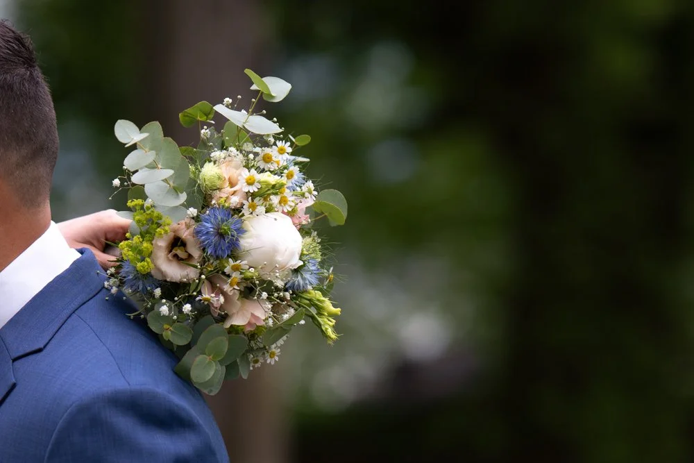 Mann in blauer Anzug hält einen Blumenstrauß hinter seinem Hals.