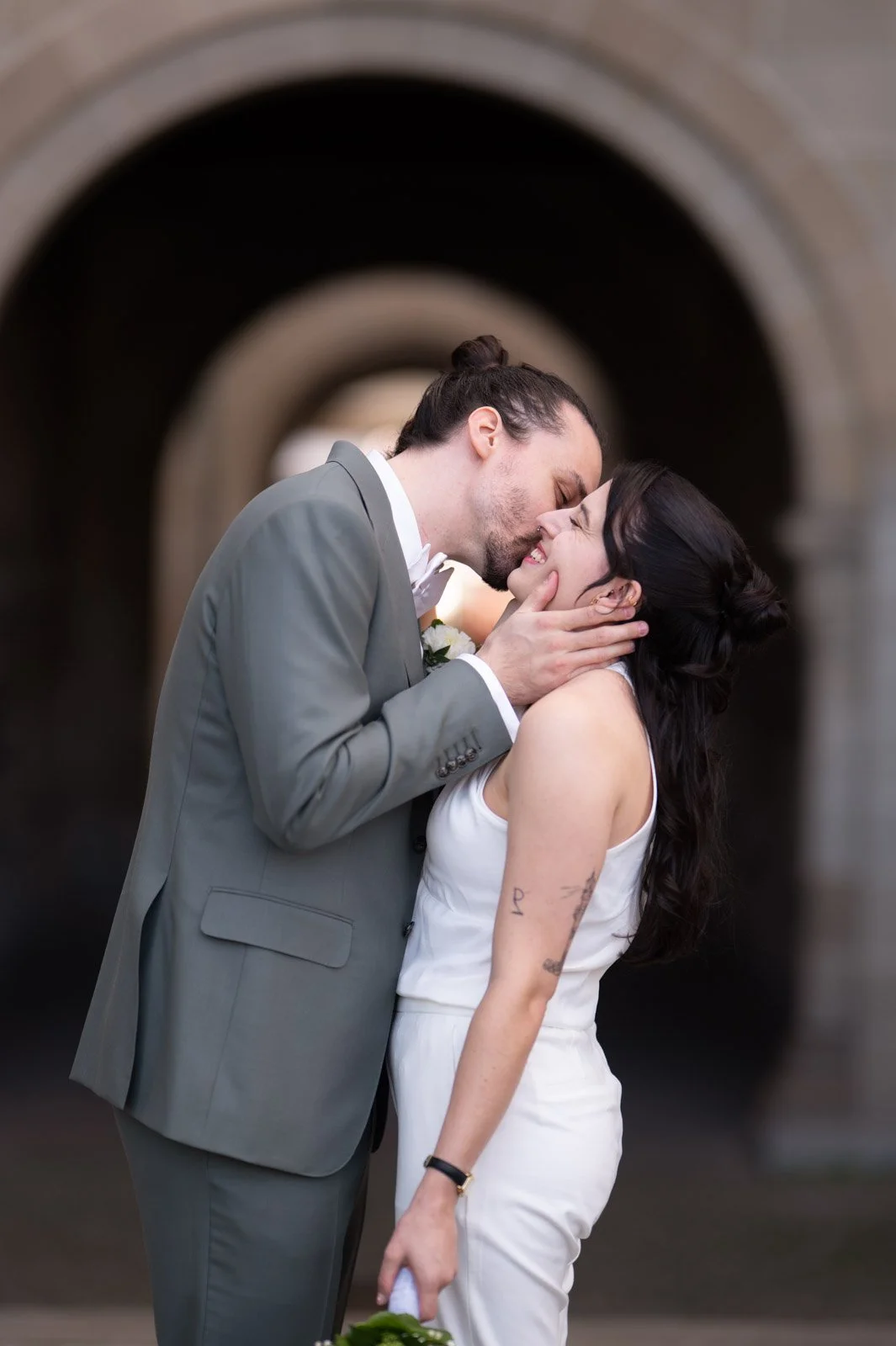 Ein glückliches Paar bei einer Hochzeit, der Mann küsst die Frau, die sich freut, bei einem historischen Gebäude im Hintergrund.