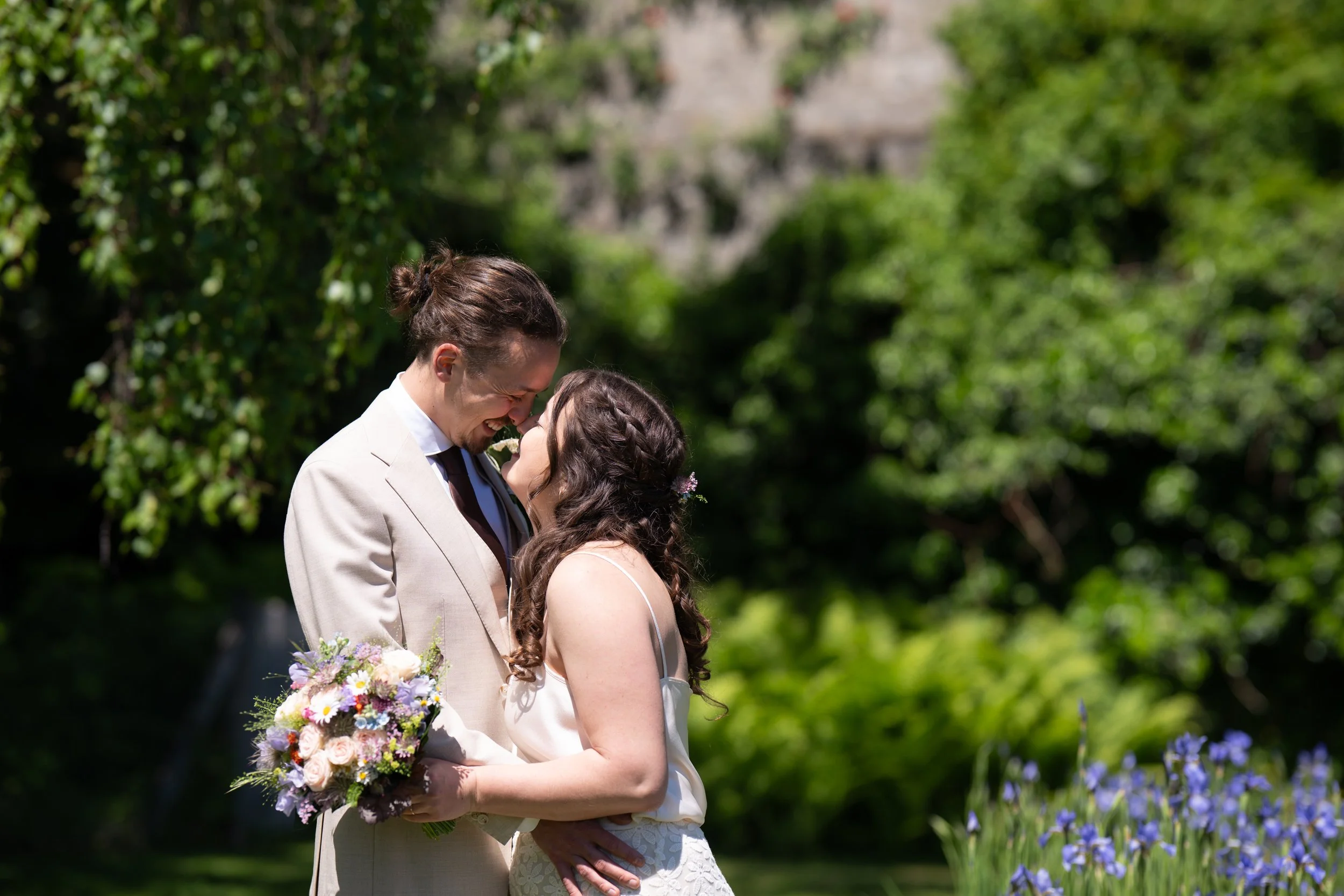 Ein Paar bei einer Hochzeit im Grünen, hält sich an den Händen und lächelt sich an.