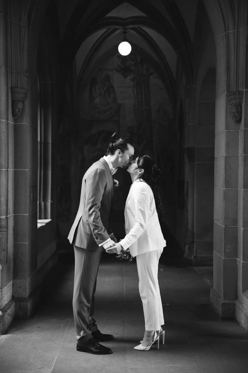 Ein Paar in formeller Kleidung küsst sich in einem gotischen Flur.