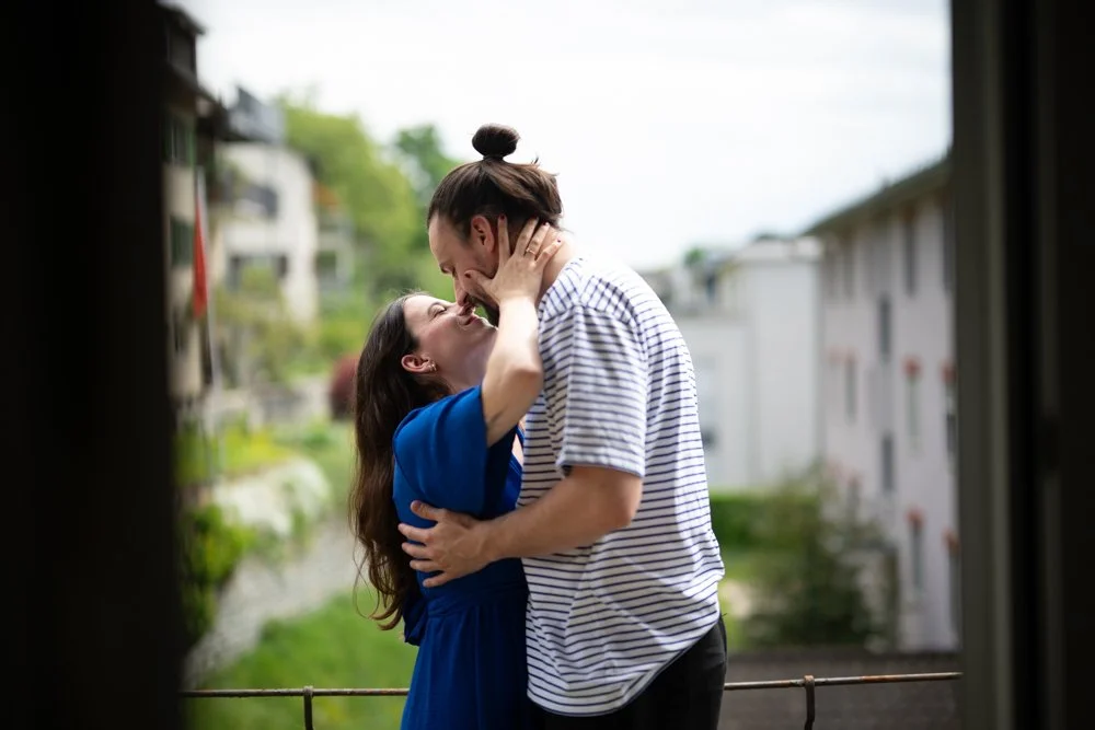 Ein Paar steht sich im Freien gegenüber, küsst sich leidenschaftlich, die Frau hält den Mann im Arm, der Mann trägt ein gestreiftes Hemd, die Frau trägt ein blaues Kleid.