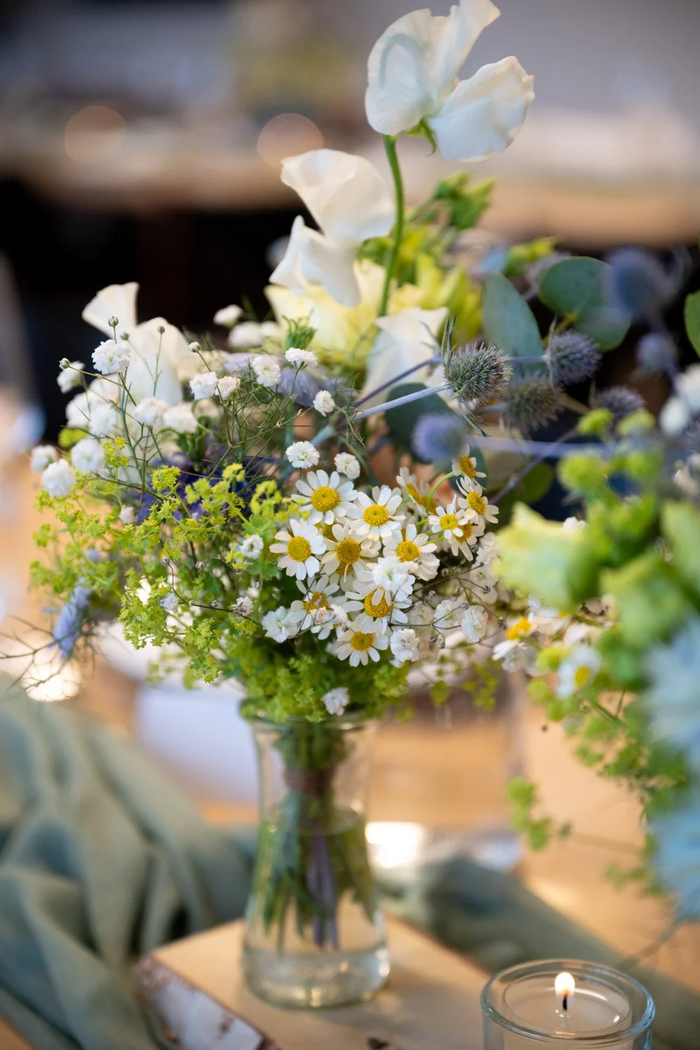 Blumenstrauß mit weißen Blumen, Gräsern und Eukalyptus in einer Glasvase auf einem Tisch mit Kerze