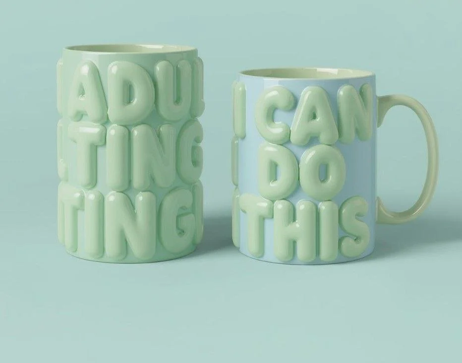 Two ceramic mugs with raised letters, one says 'ADULTING' and the other says 'I CAN DO THIS'.