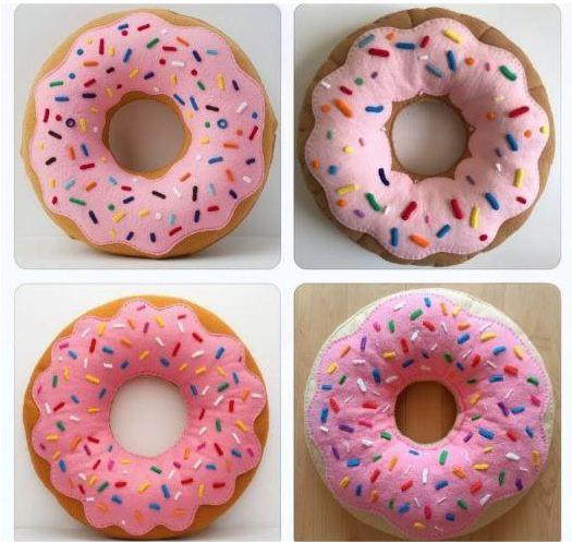 Four donuts with pink icing and colorful sprinkles, placed on white and wooden surfaces.