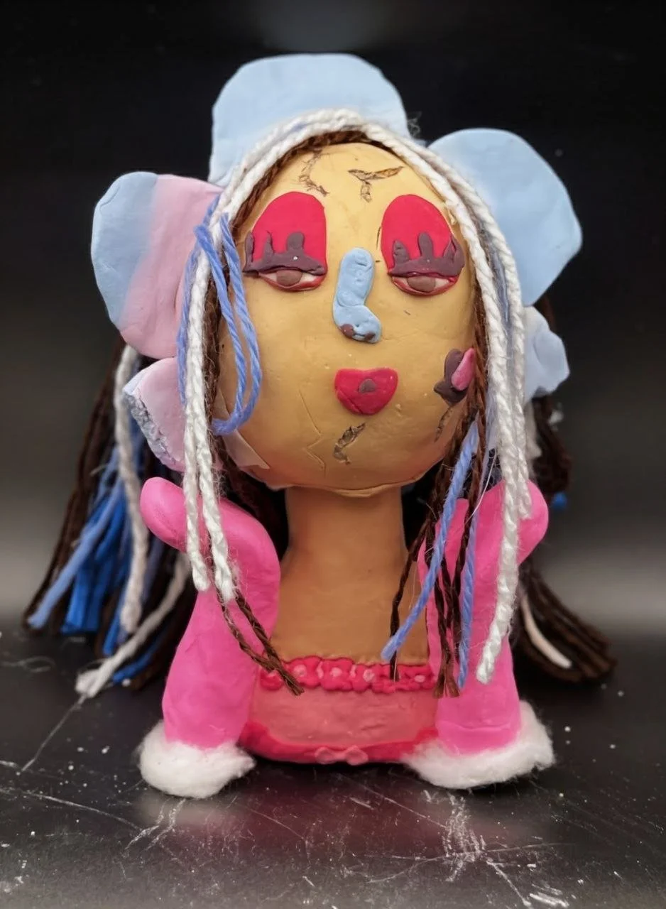A handcrafted doll with a painted face, long yarn hair, and clothing made of fabric and yarn.