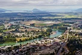 Aerial view of a city with roads, a river, and surrounding green fields.