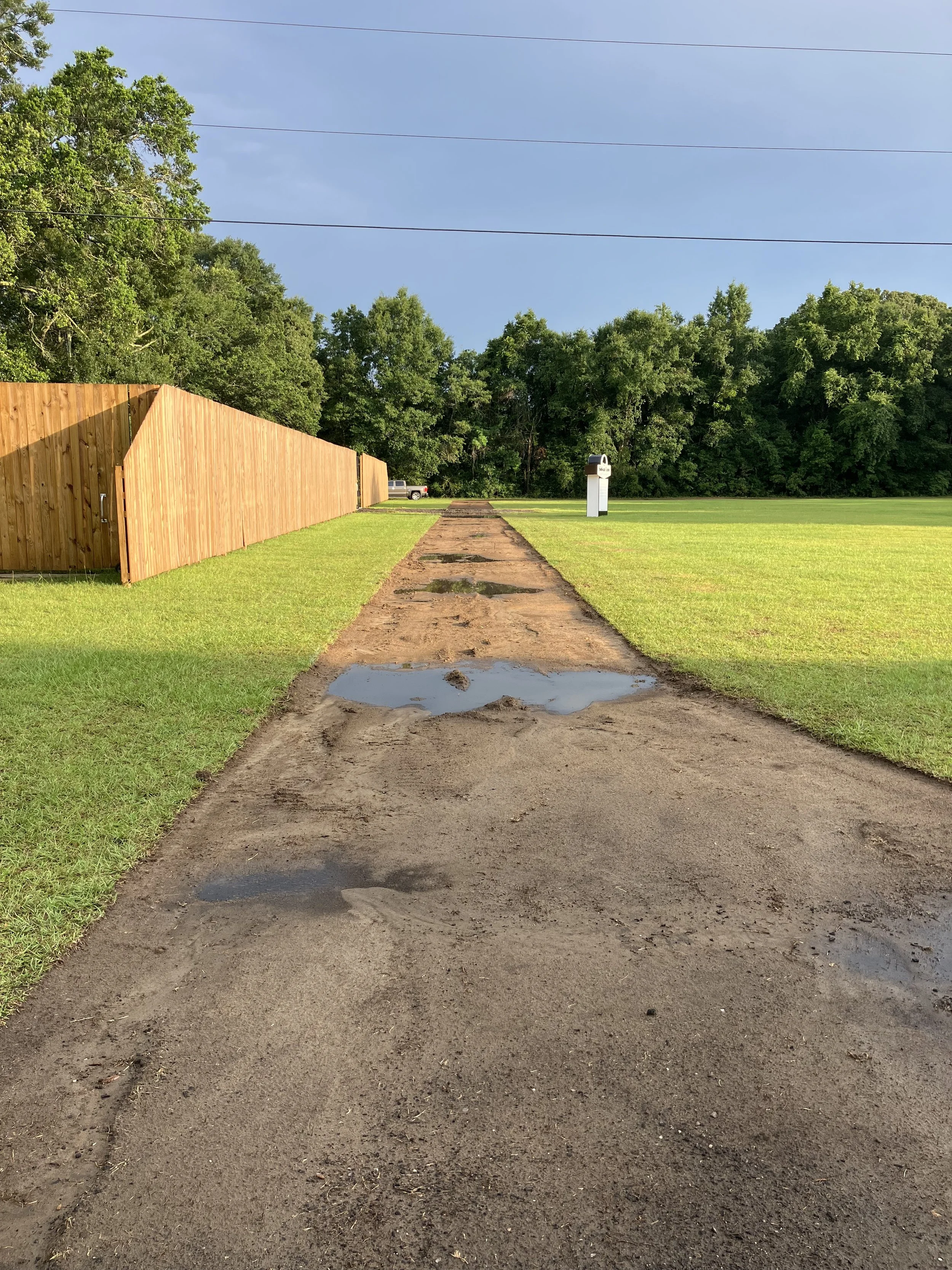 green grass bordering prepped new gravel driveway under blue sky