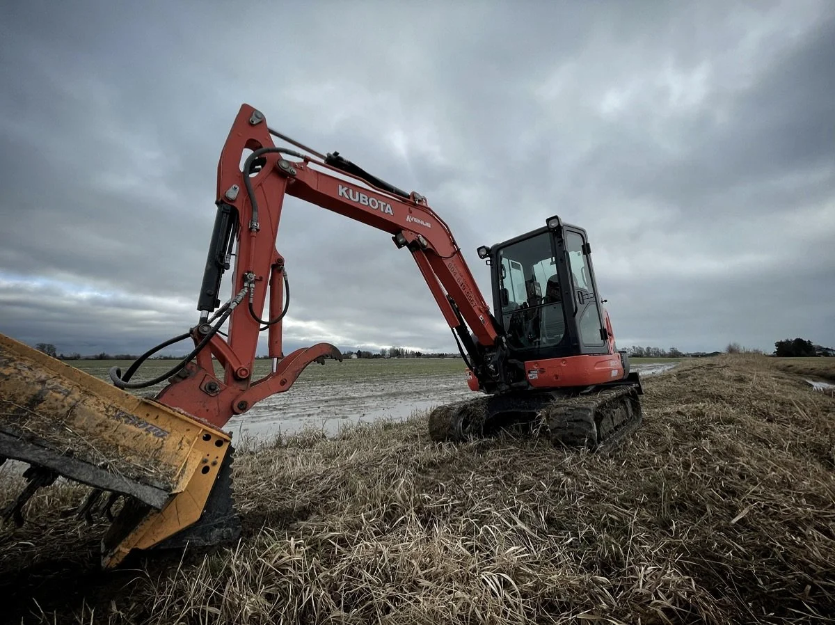 Red Kubota compact excavator working in a farm field under cloudy sky.