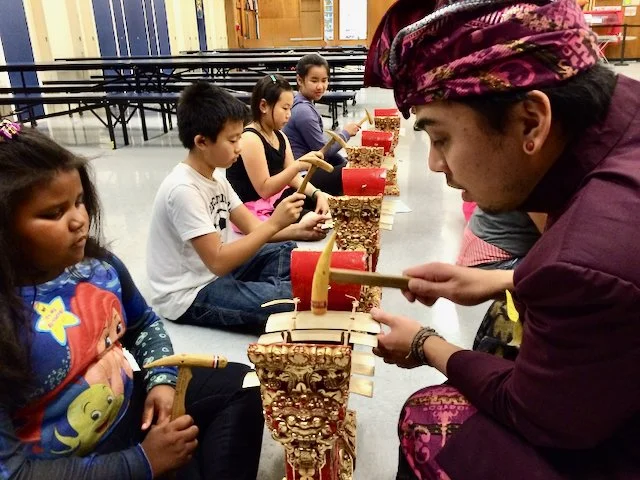 Children and an adult playing traditional musical instruments in a classroom or community center setting.