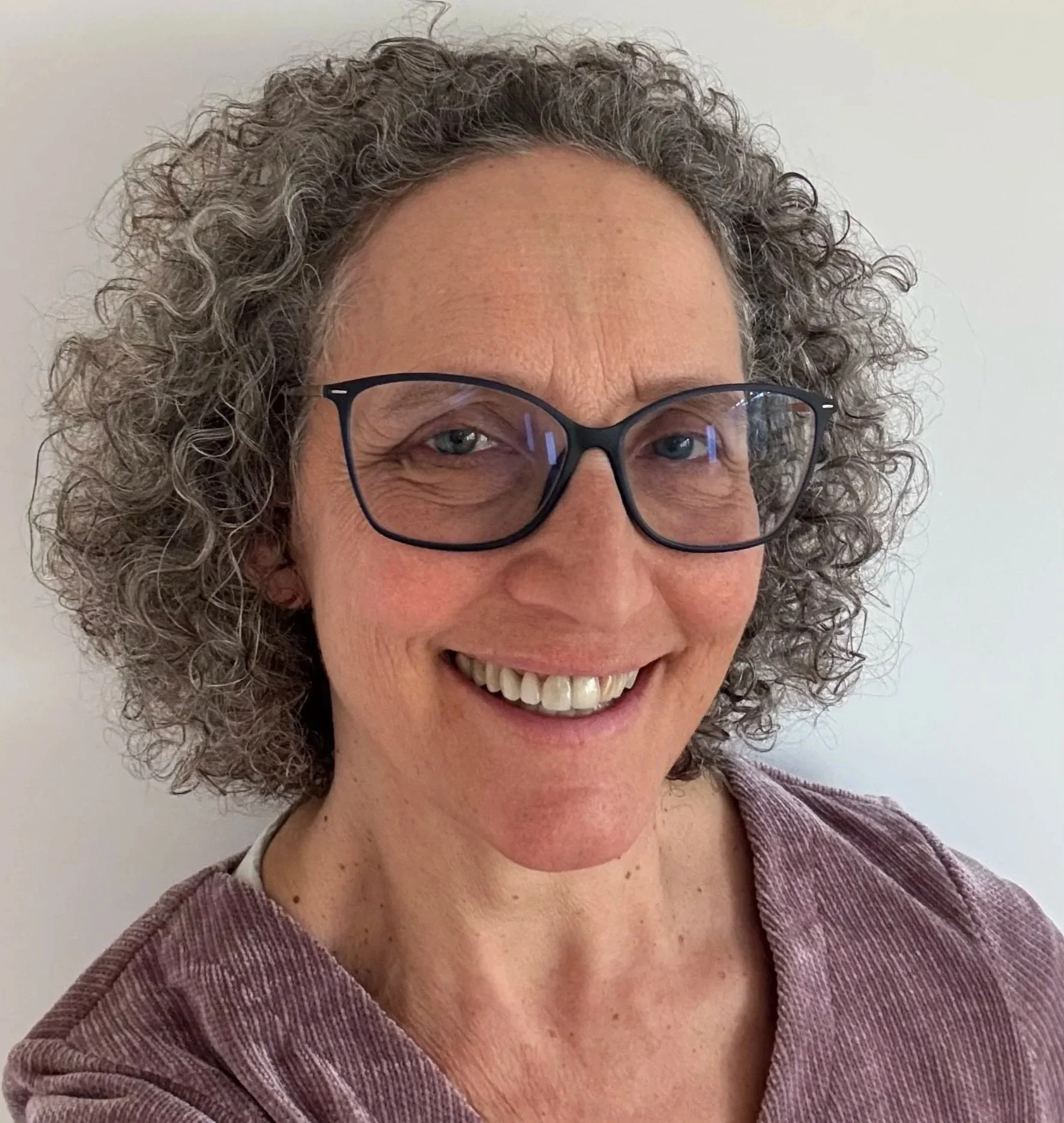 A woman with curly gray hair wearing glasses and smiling at the camera.