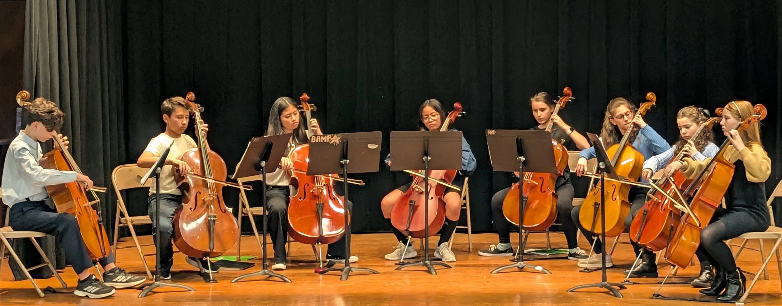 A group of children playing cellos on a stage during a performance.