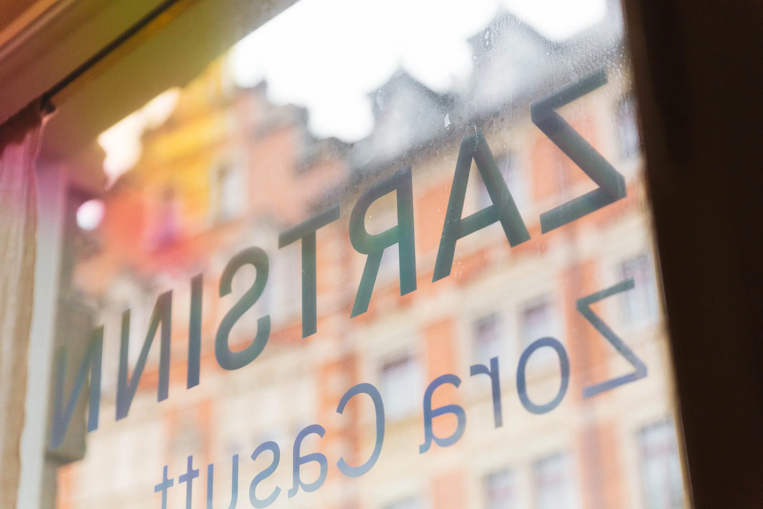 Fenster mit geschriebener Beschriftung »Artisan Backstube«, Blick auf eine Stadt im Hintergrund.