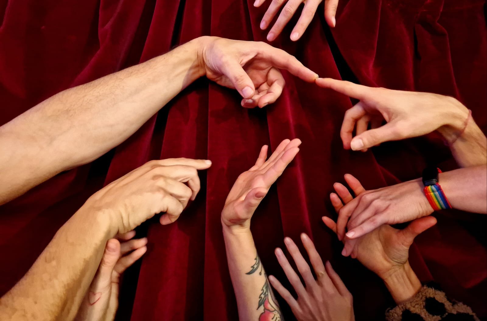 Mehrere Hände verschiedener Menschen, die miteinander interagieren, auf rotem Stoffhintergrund. Ein Symbol für den Konsens Workshop der in St.Gallen stattfindet.