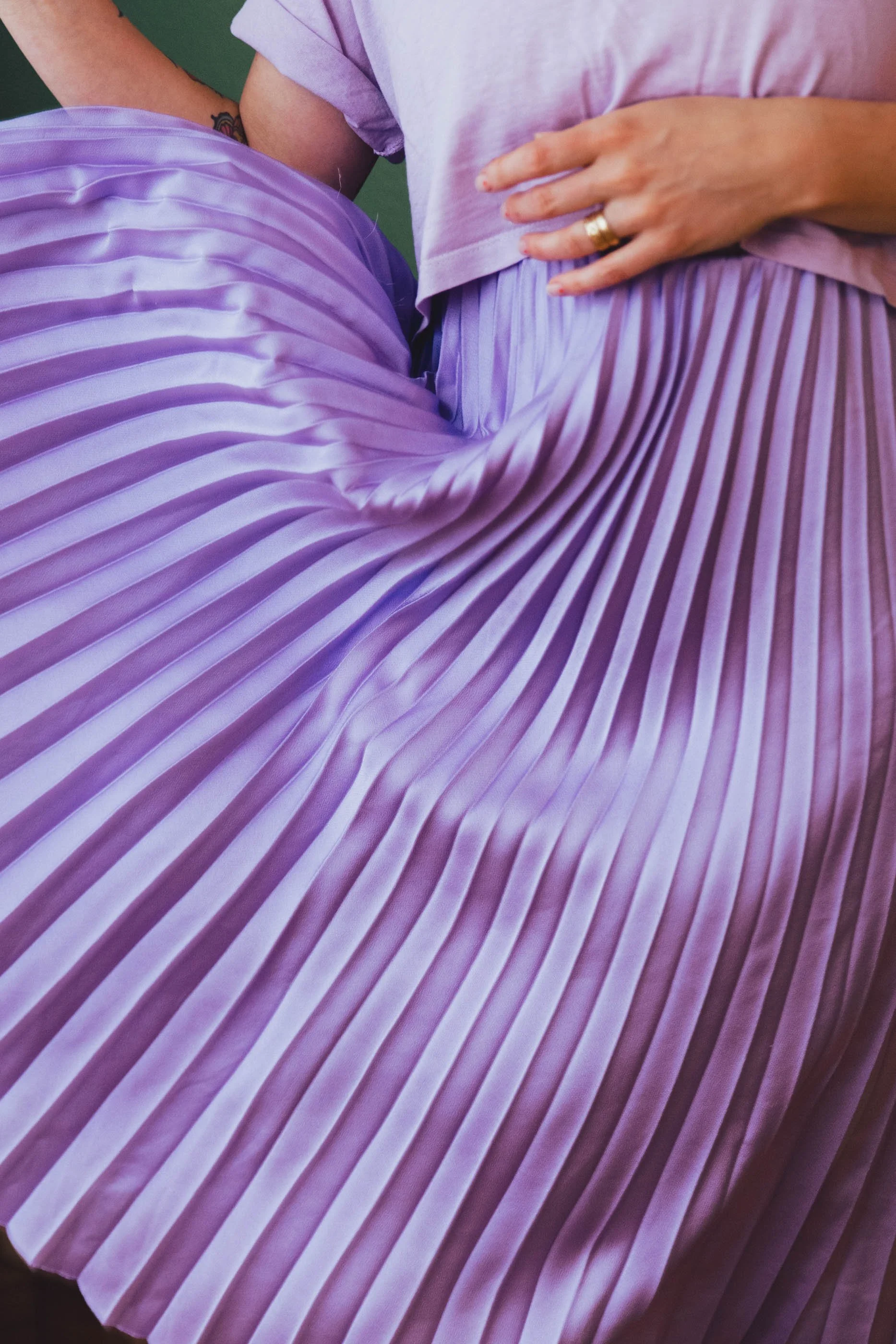 Nahaufnahme eines violetten, plettierten Stoffes, getragen von einer Person. Teil des Oberkörpers, Hand und Kleid zu sehen. Ein Sinnbild für Sinnlichkeit. Dieses Bild ist Teil des weiblich sein Workshops von ZARTSINN in st.gallen.