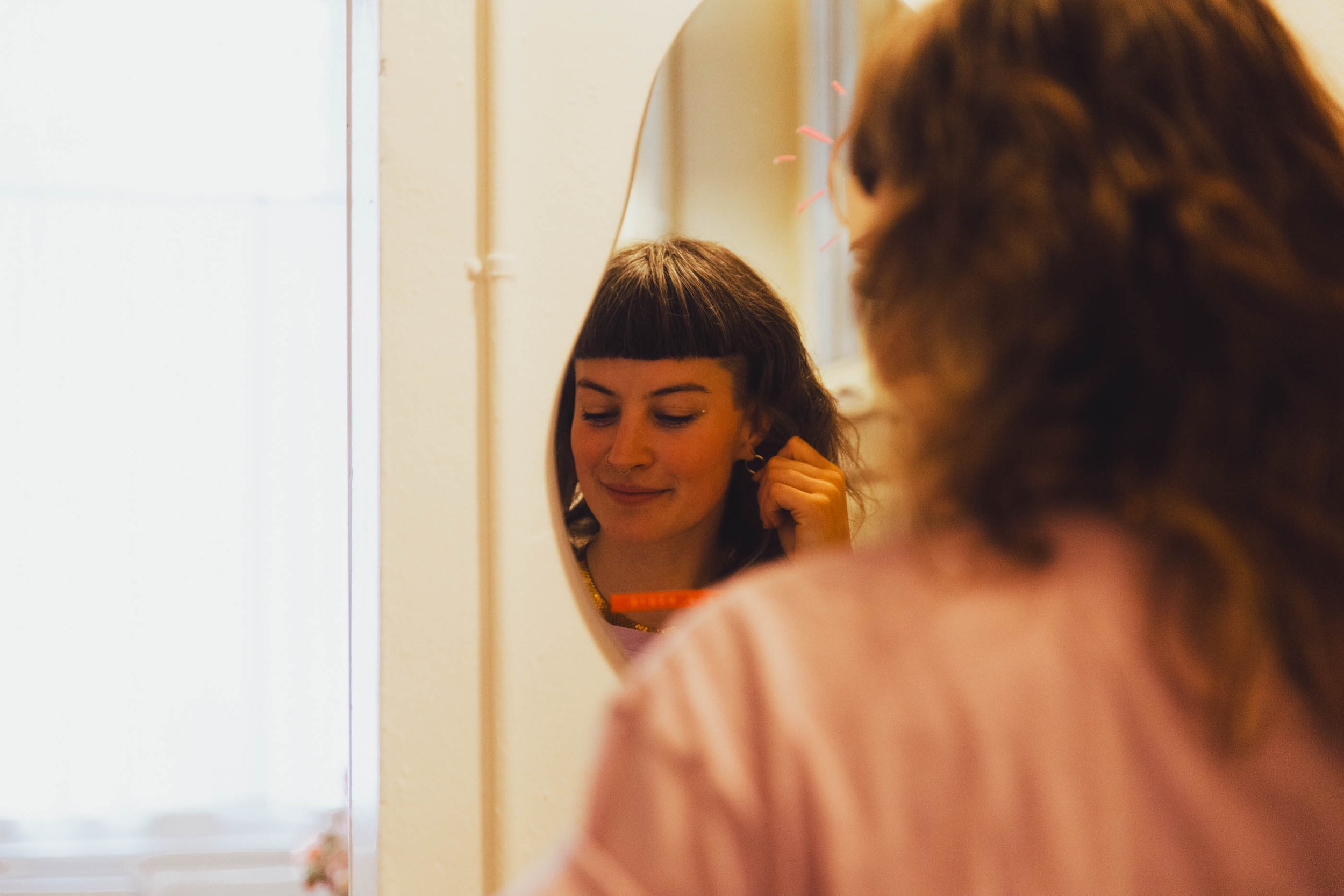 Eine junge Frau schaut in einen Spiegel, während sie sich die Ohrringe einkleidet. Ein sxmbol für den weiblich sein Workshop von ZARTSINN.