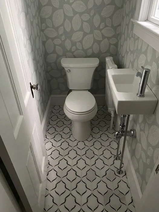 Small bathroom with wallpaper featuring leaf pattern, a toilet, and a tiny wall-mounted sink with a modern faucet.