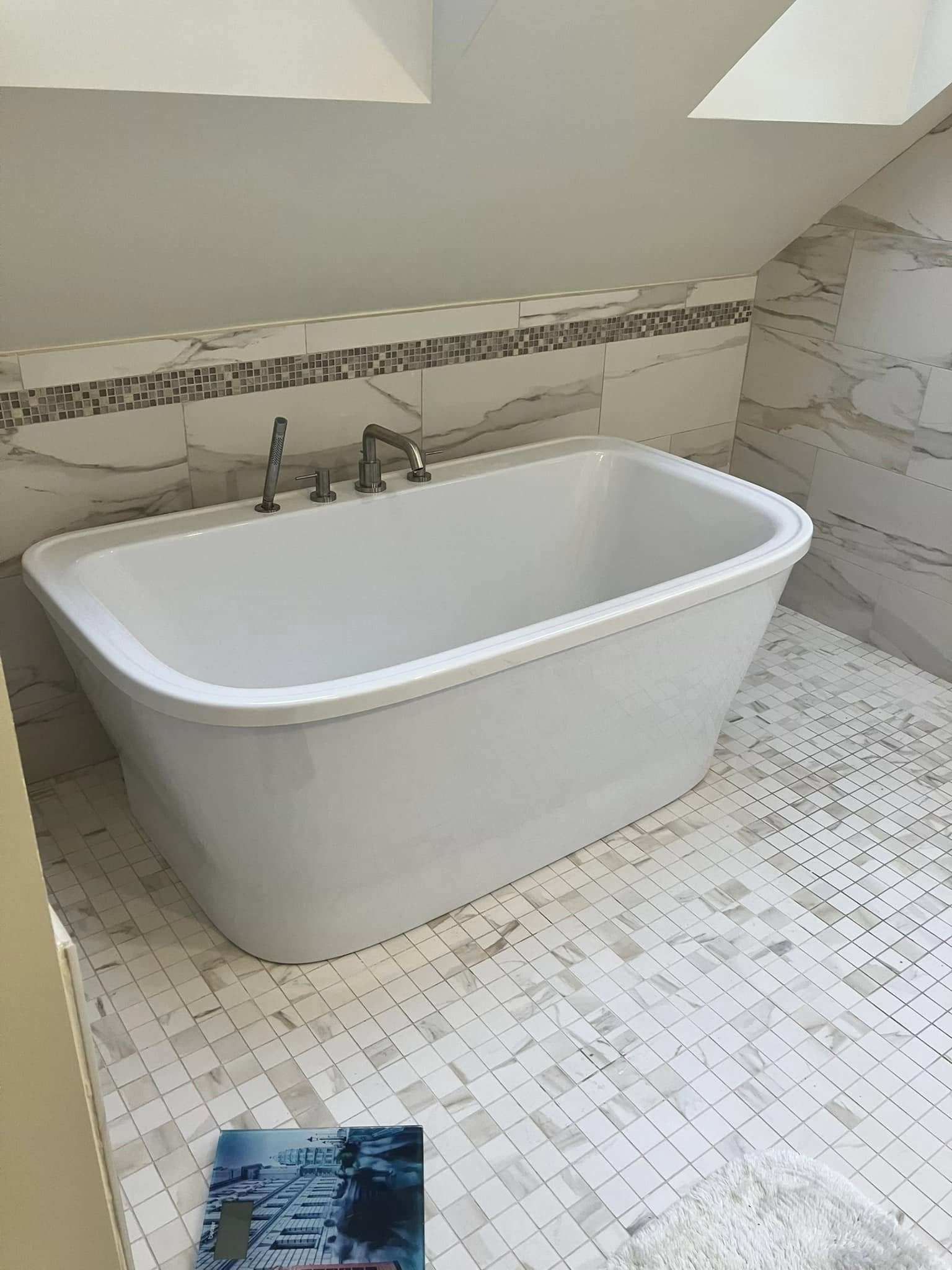 White bathtub with silver faucet and handles in a bathroom with tiled walls and floor.