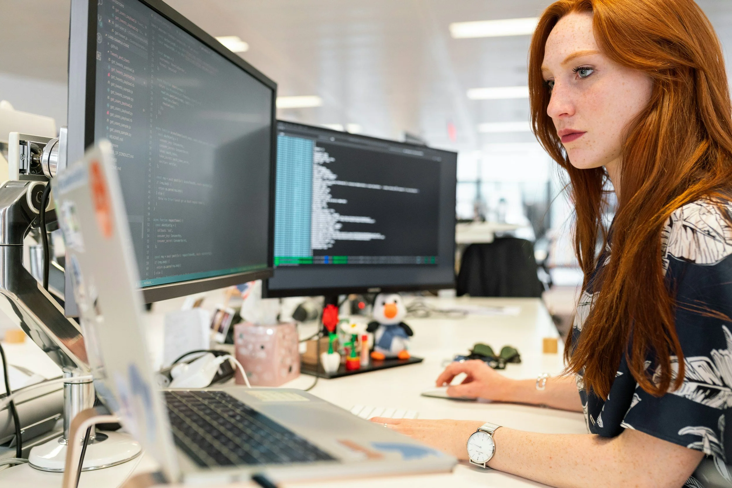Woman working at a computer with two monitors in an office.
