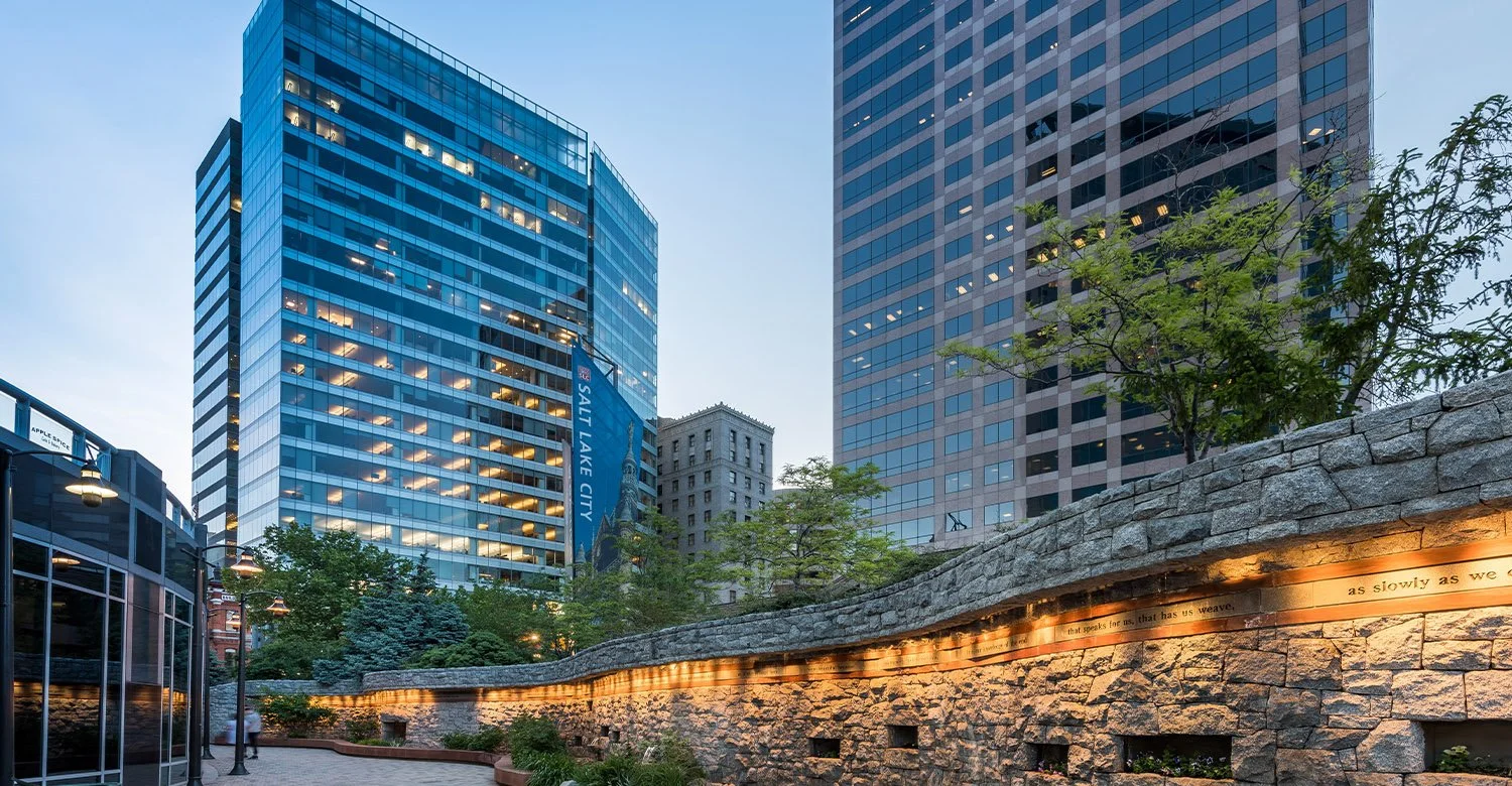 Urban park with stone wall and trees in front of modern high-rise buildings with glass facades
