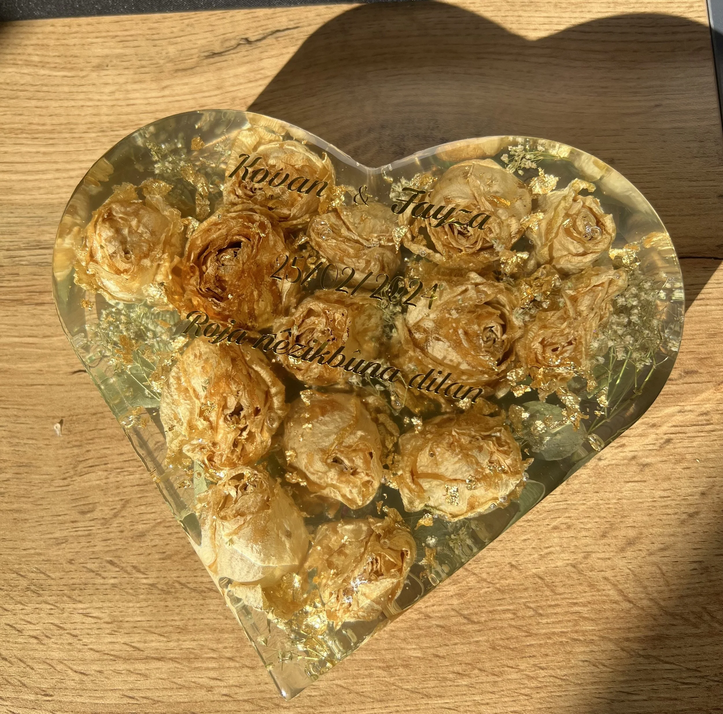 Cœur en verre contenant des roses en papier doré avec des inscriptions en français, incluant des noms, une date et une mention