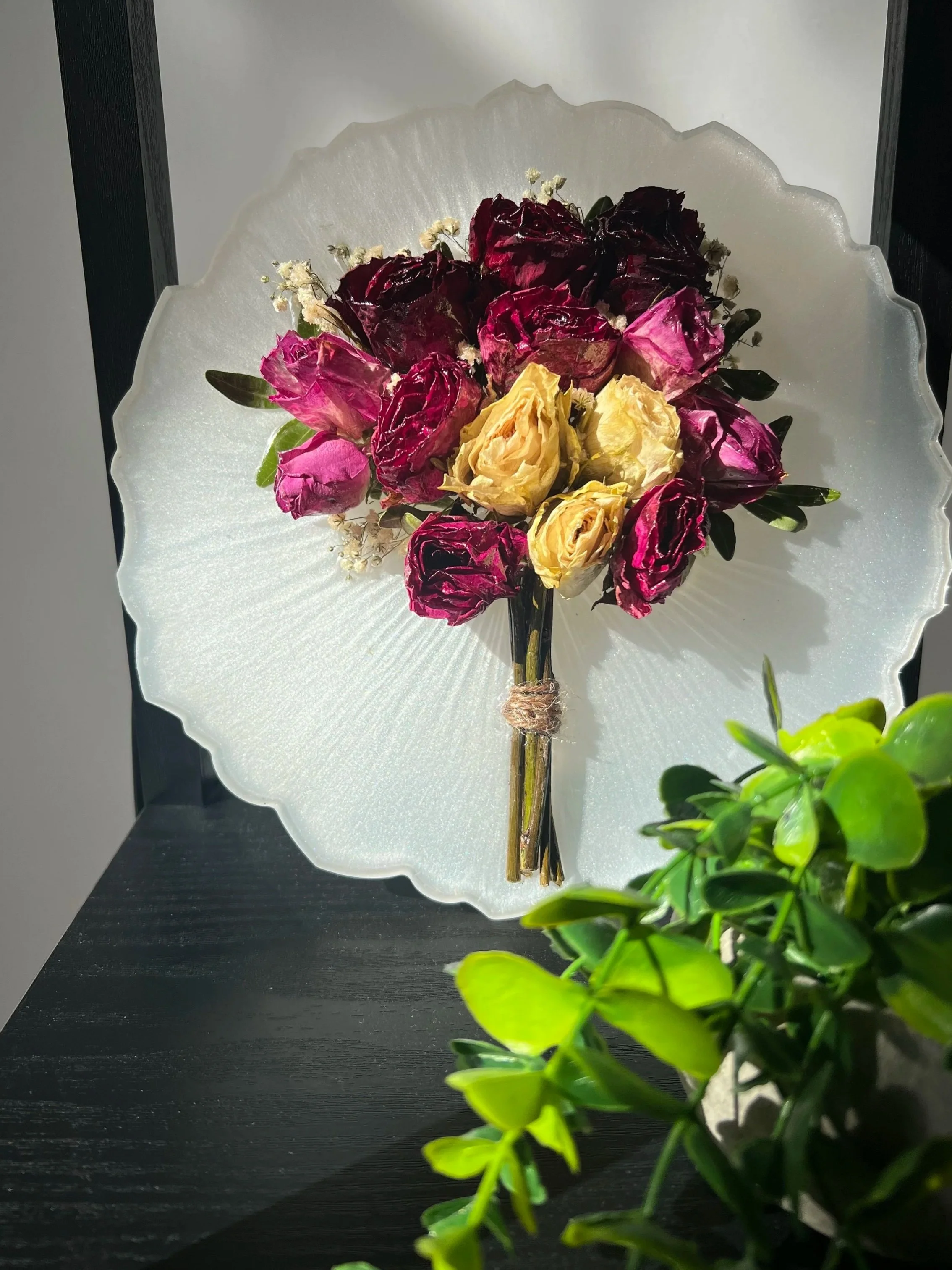 Un bouquet de fleurs séchées, principalement roses de différentes couleurs, placé sur une assiette en verre translucide avec un motif rayonnant