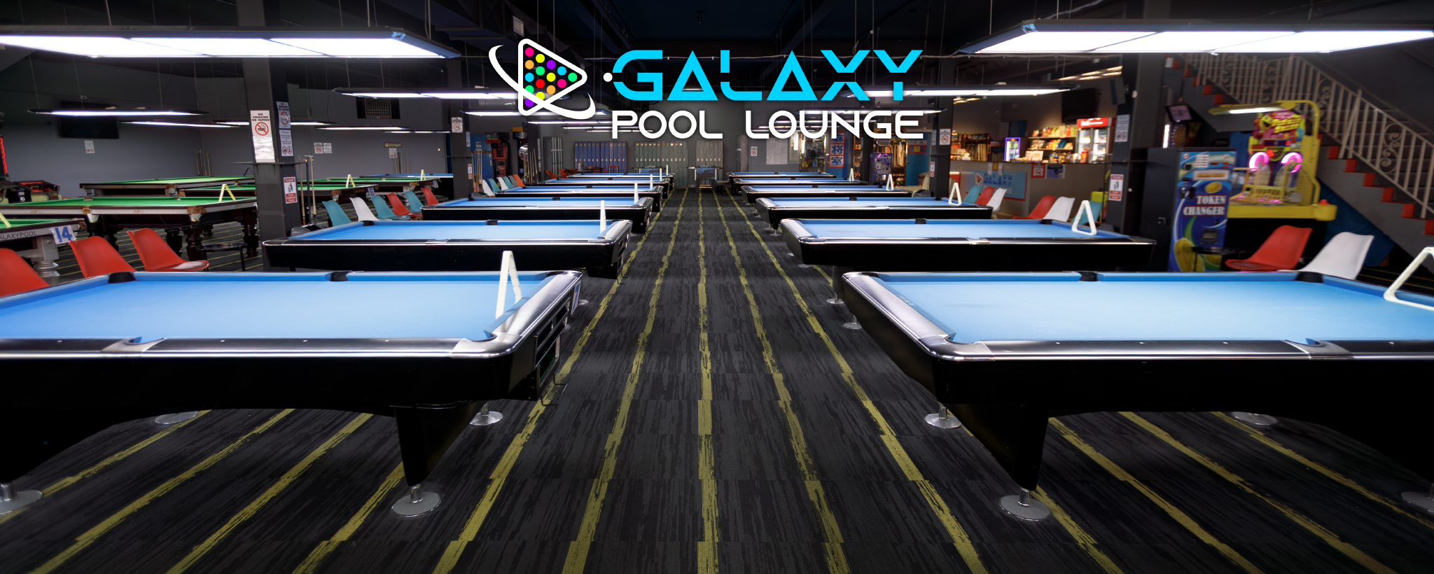 Indoor pool lounge with multiple American pool tables, seating areas, arcade games and a sign that reads 'Galaxy Pool Lounge'.