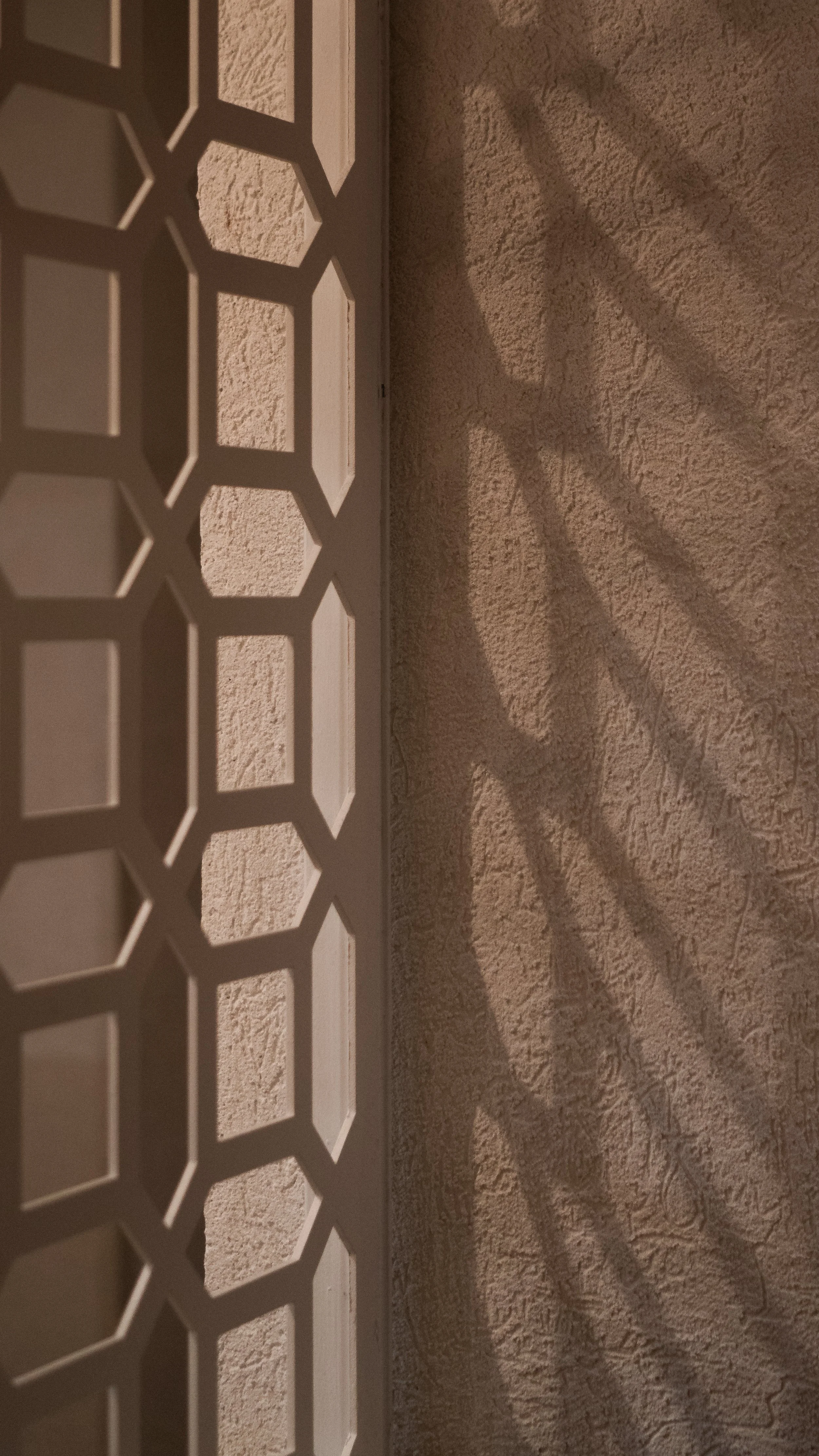 A decorative panel with a geometric honeycomb pattern, casting a shadow on a textured wall.