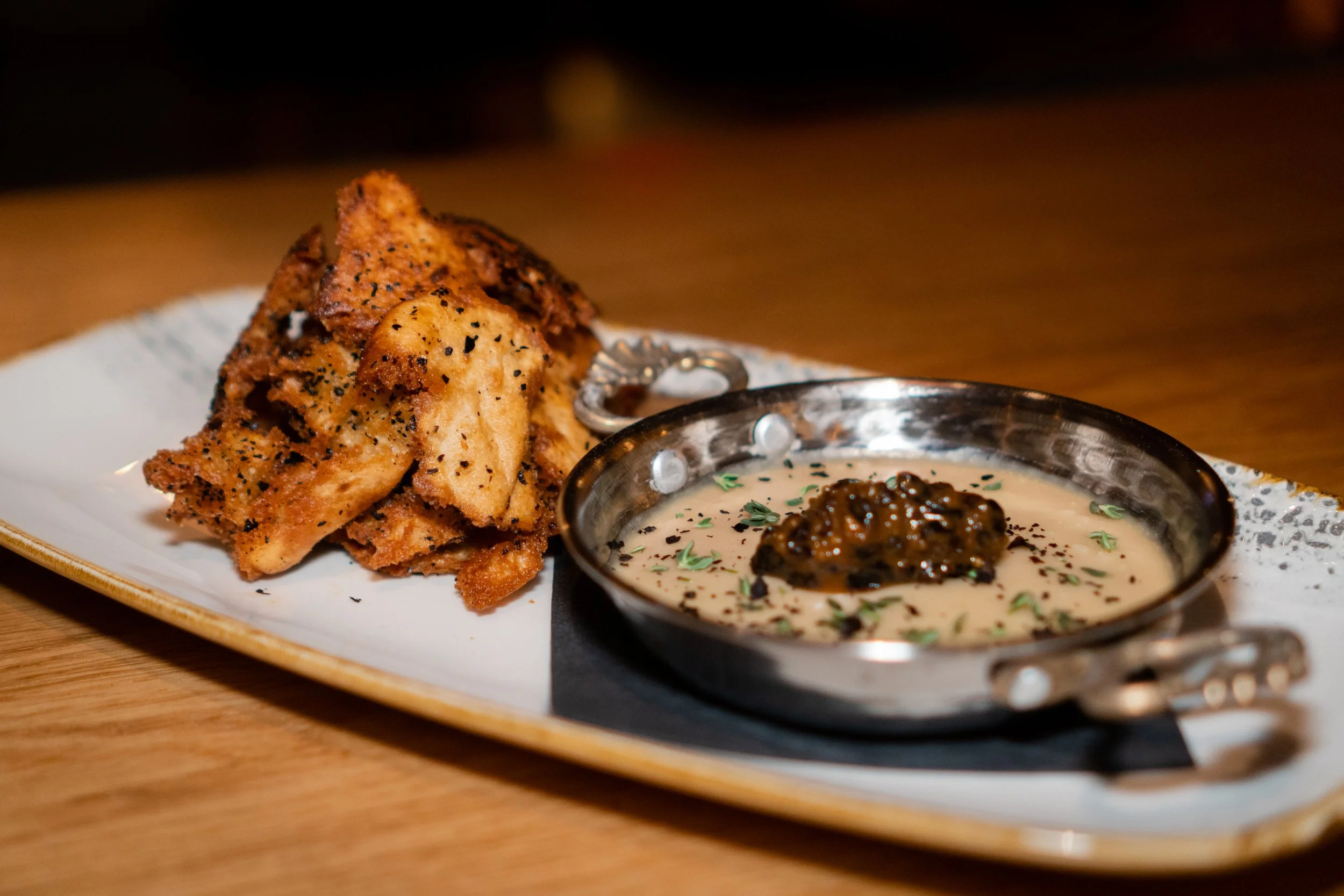 Fried chicken wings with black pepper served with dipping sauce in a metal bowl on a white rectangular plate.