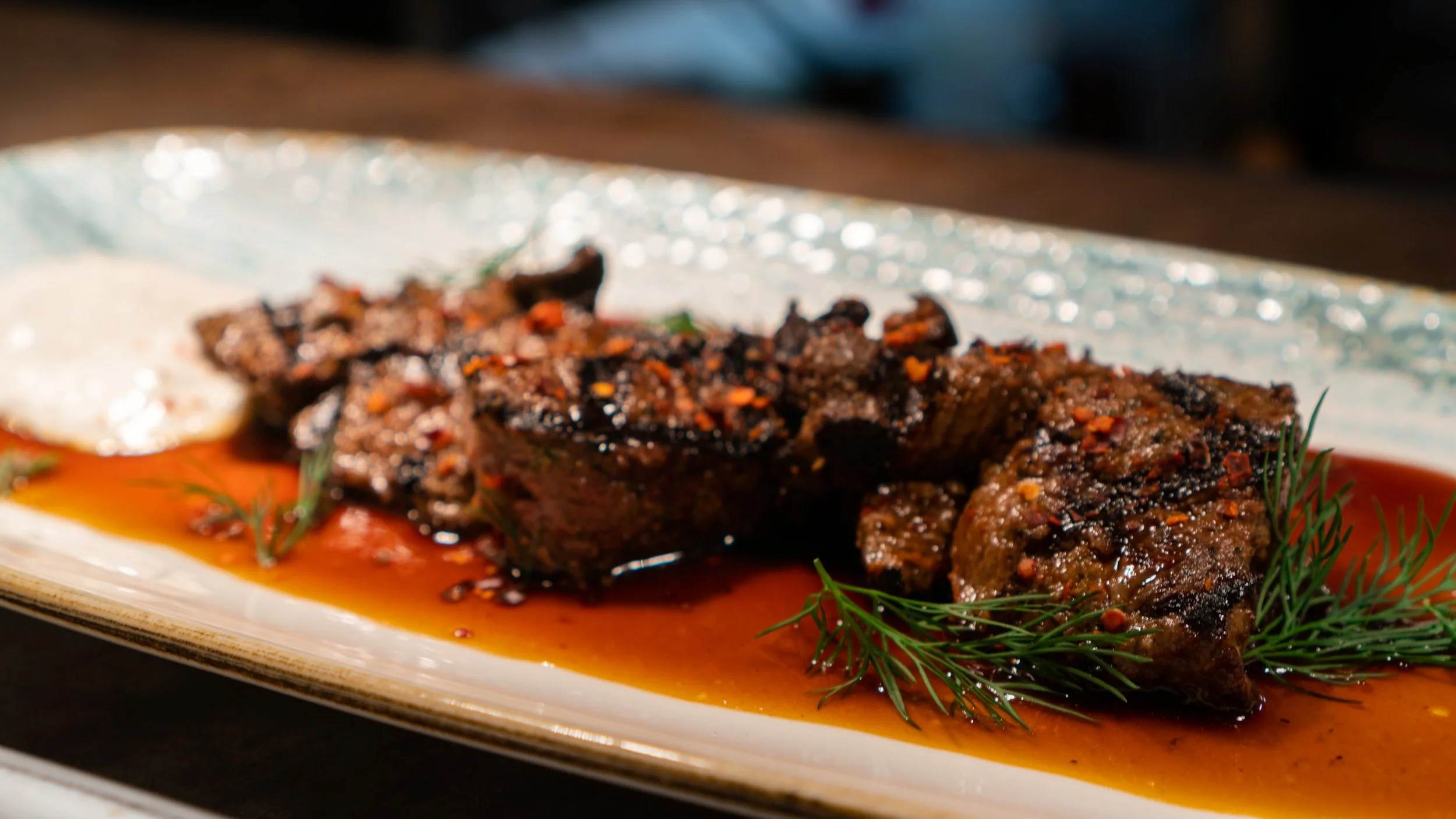 Grilled beef steak with a brown sauce, garnished with fresh dill, served on a ceramic plate.