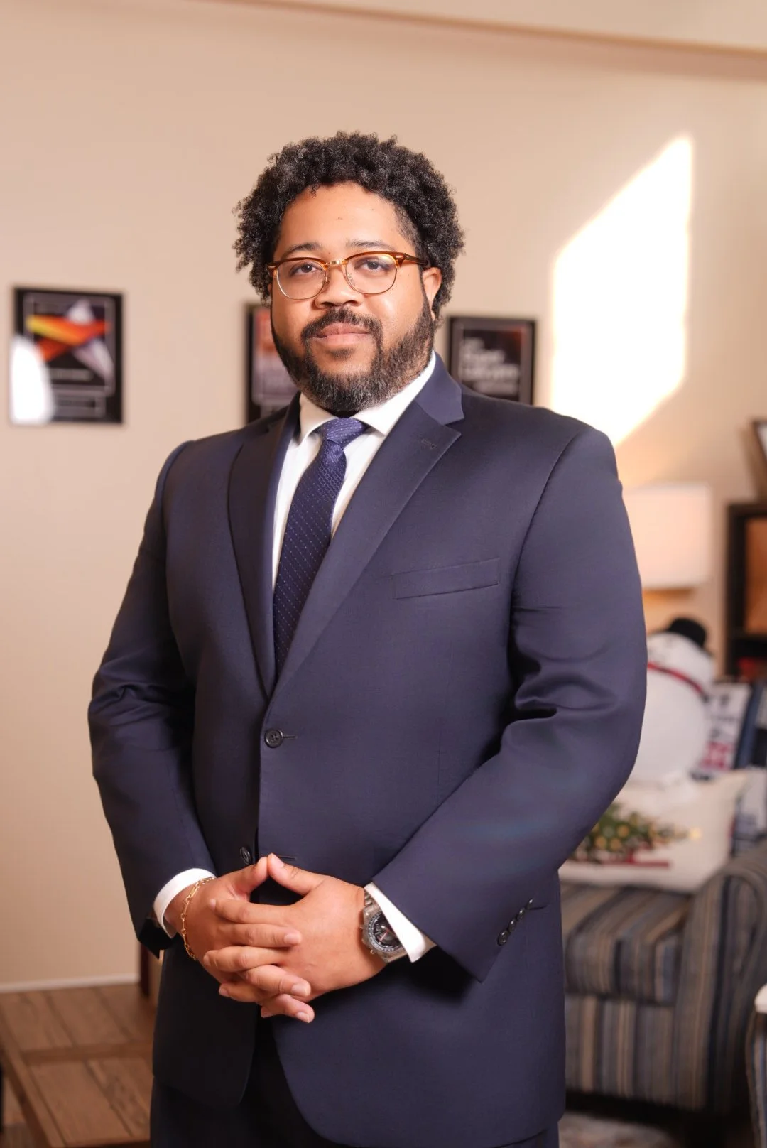 A man with curly hair wearing a blue suit with clasped hands.