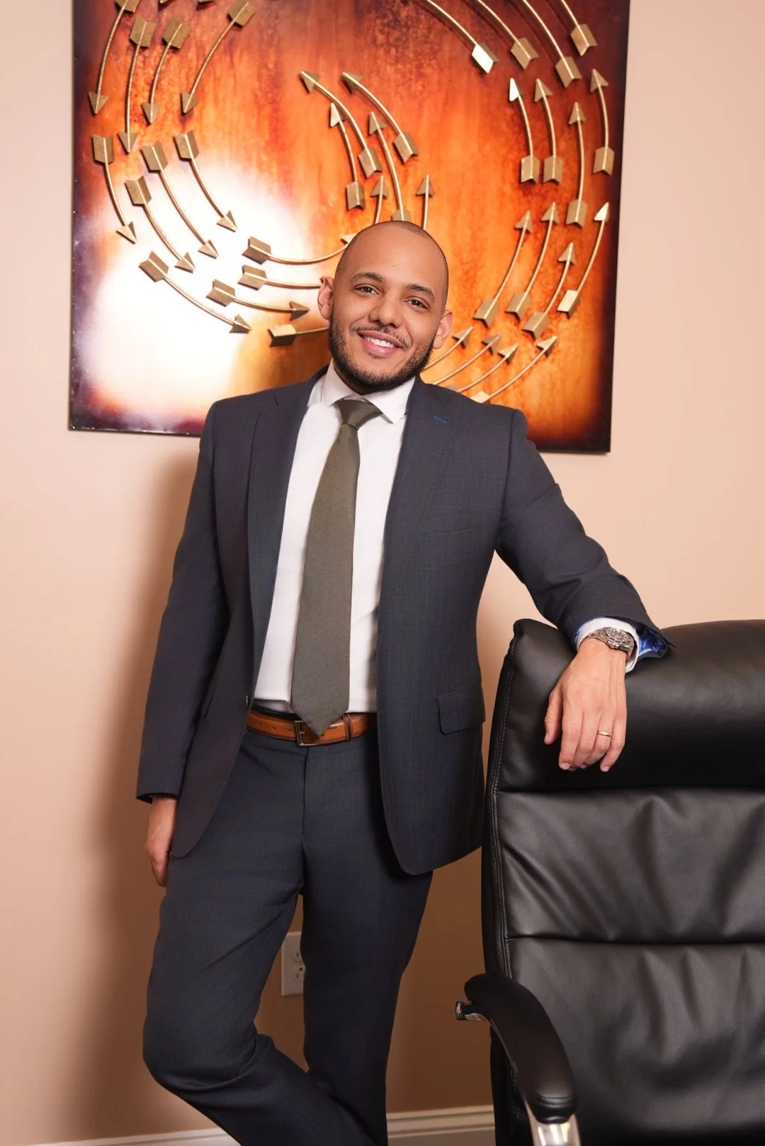 A man leaning against a chair wearing a suit.