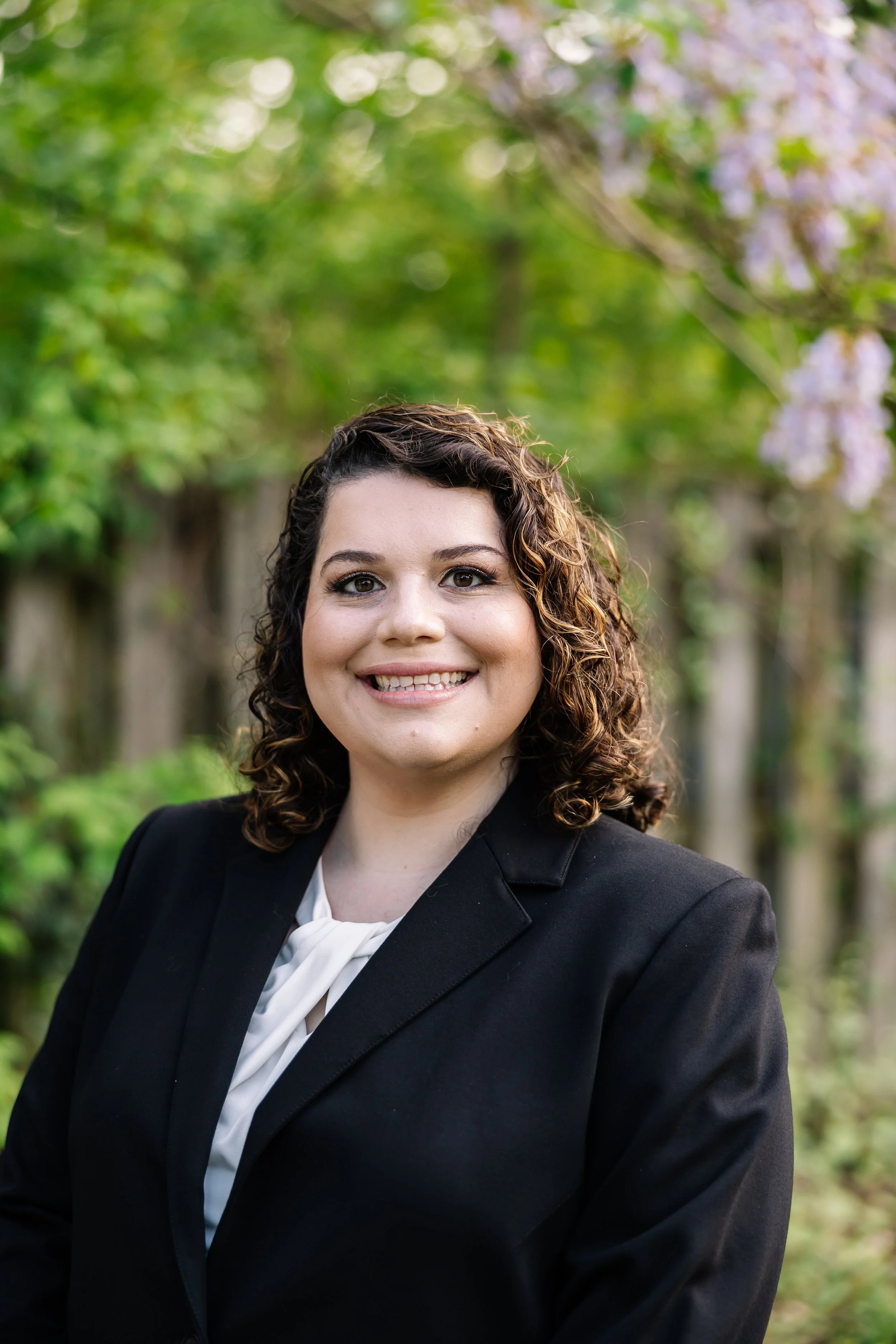 Picture of a Marissa Lelii, Esquire smiling at the camera with curly brown hair wearing a black suit jacket.