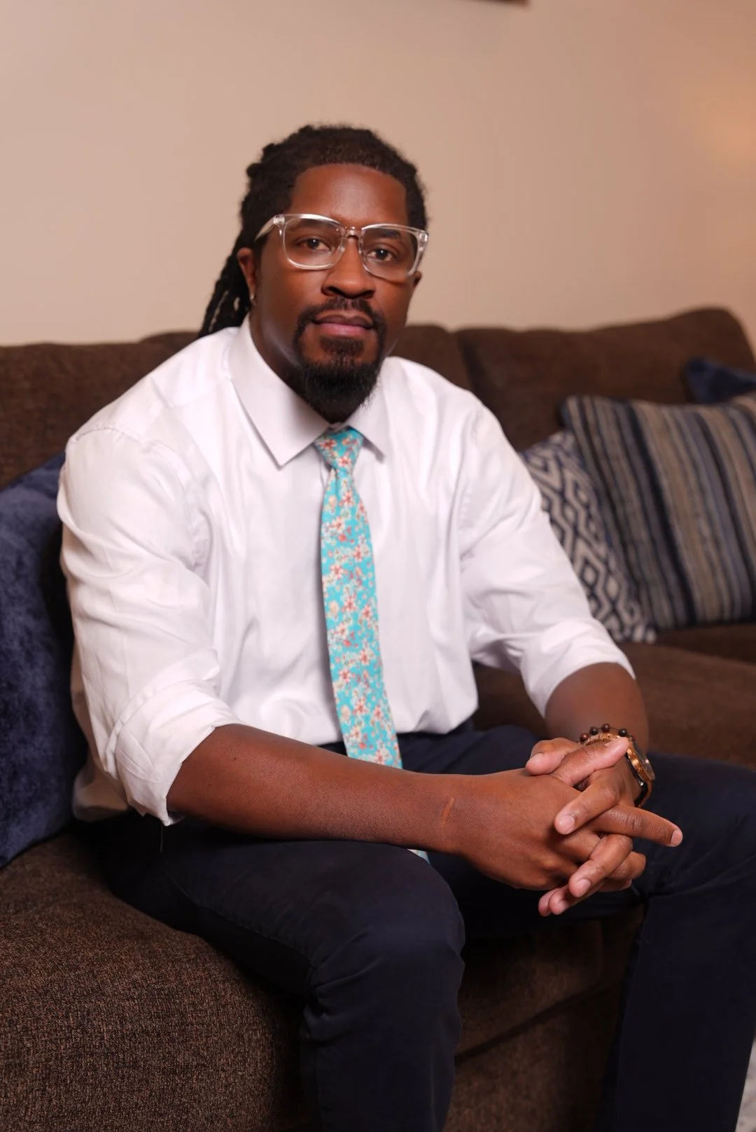 A young man with glasses on sitting on the couch.