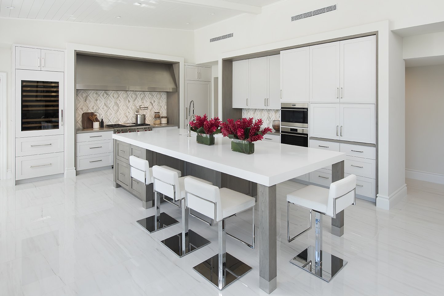 Modern white kitchen with a large island, white barstools, and built-in appliances, decorated with pink flowers.
