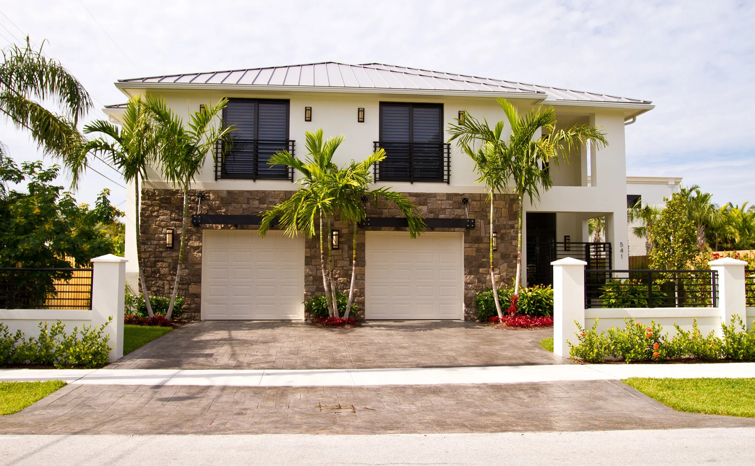 Modern two-story house with white exterior, stone accents, black shutters, and palm trees in the front yard.