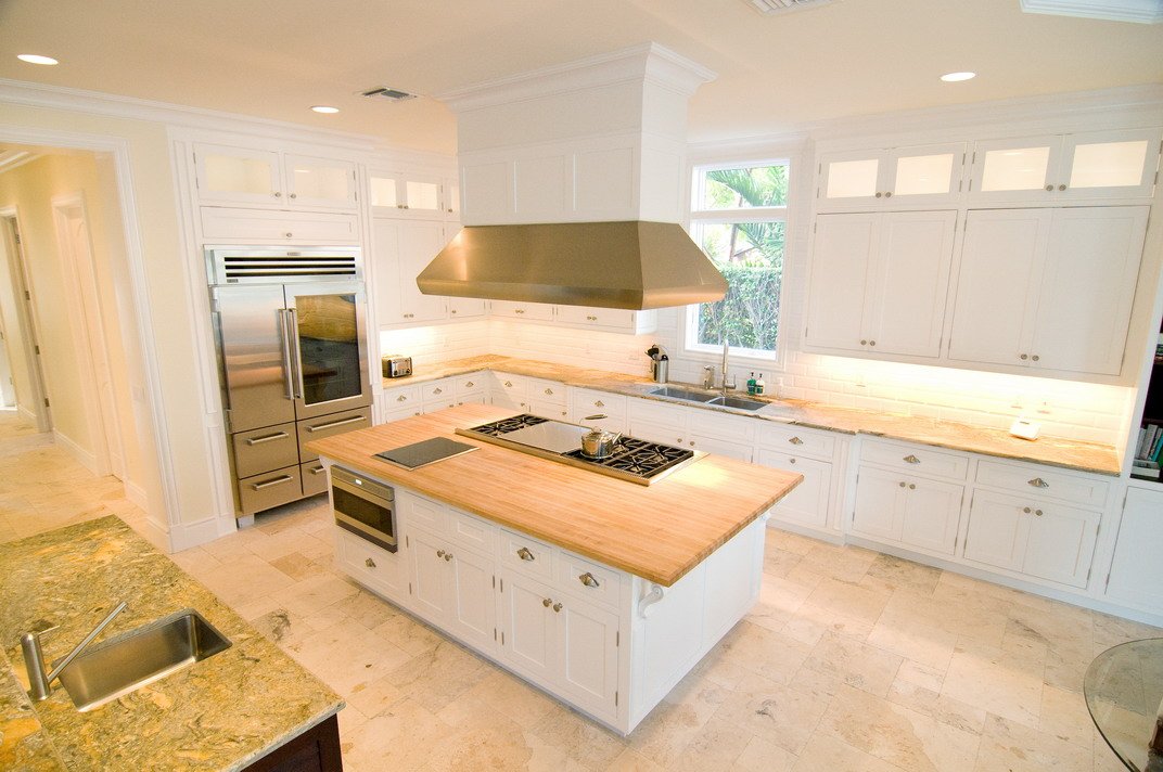 Bright, white kitchen with a center island, stainless steel appliances, and natural wood countertops.