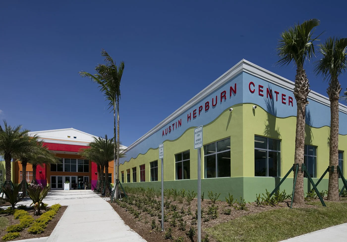 Colorful building with the sign 'Austin Hepburn Center' with palm trees in front and a clear blue sky.