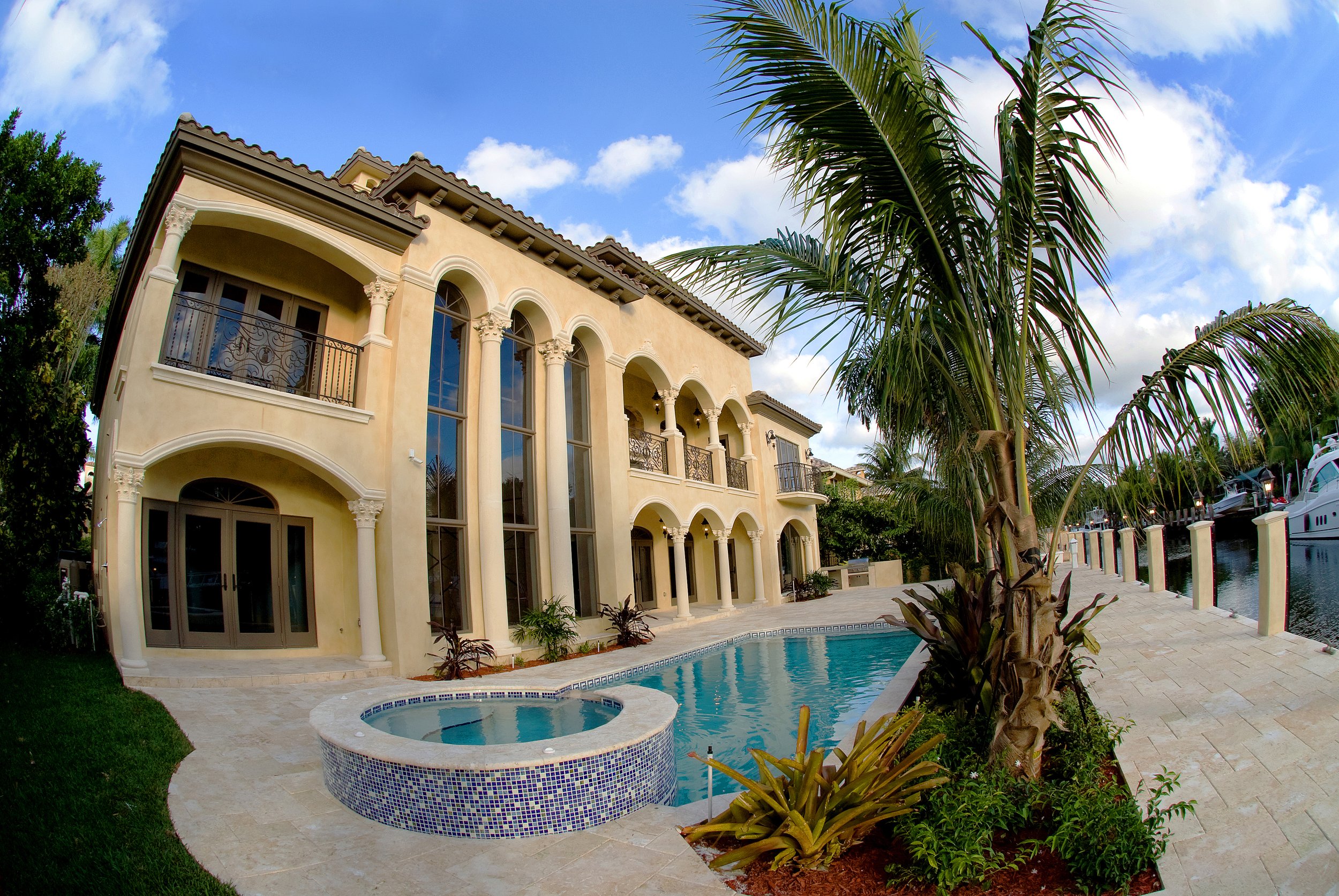Luxury house with a swimming pool and hot tub, palm trees, and a waterway with boats