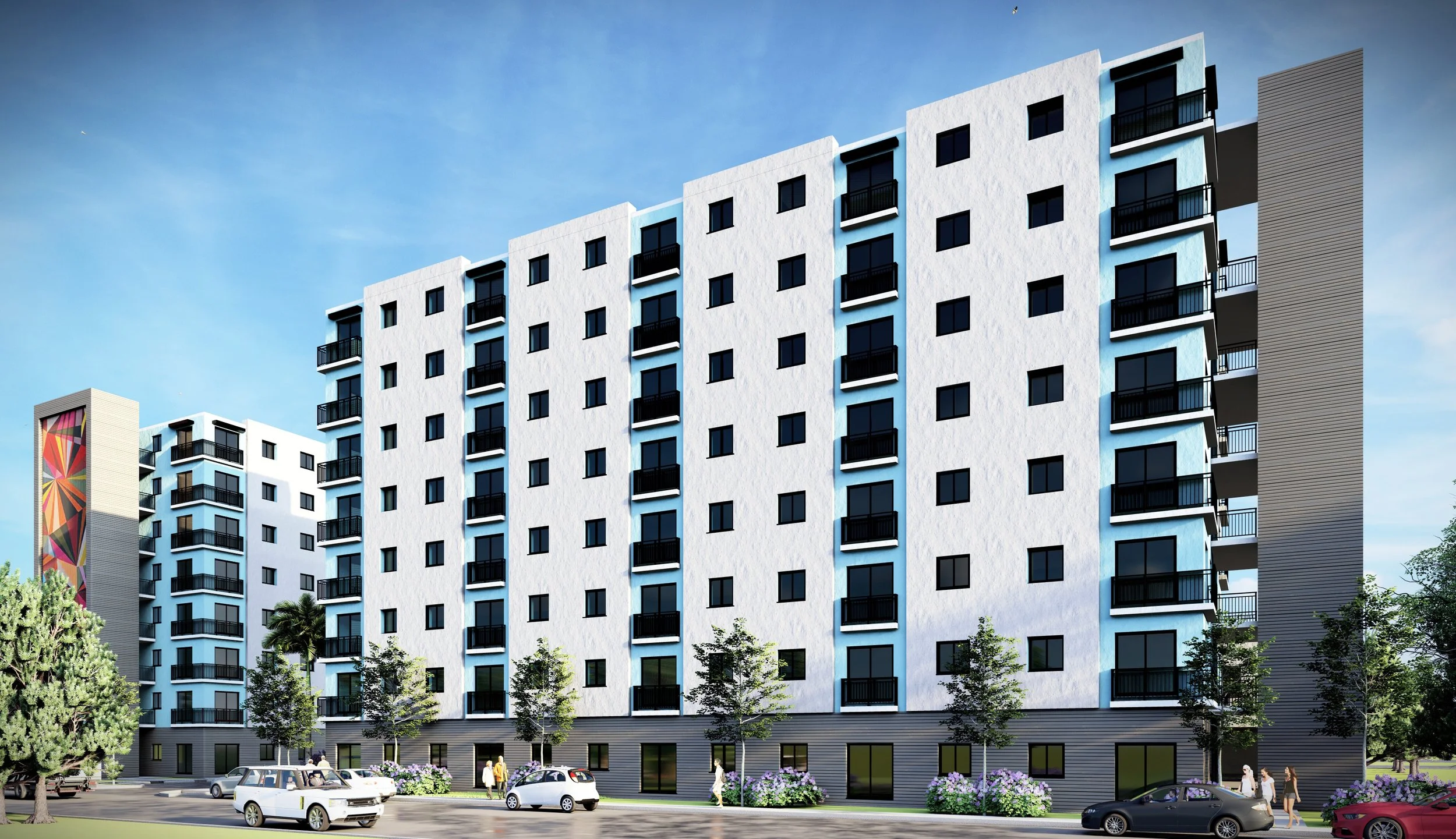 Modern white mid-rise apartment building with balconies, black railings, landscaped ground, parking area, pedestrians, trees, and colorful mural on adjacent building, under a blue sky.