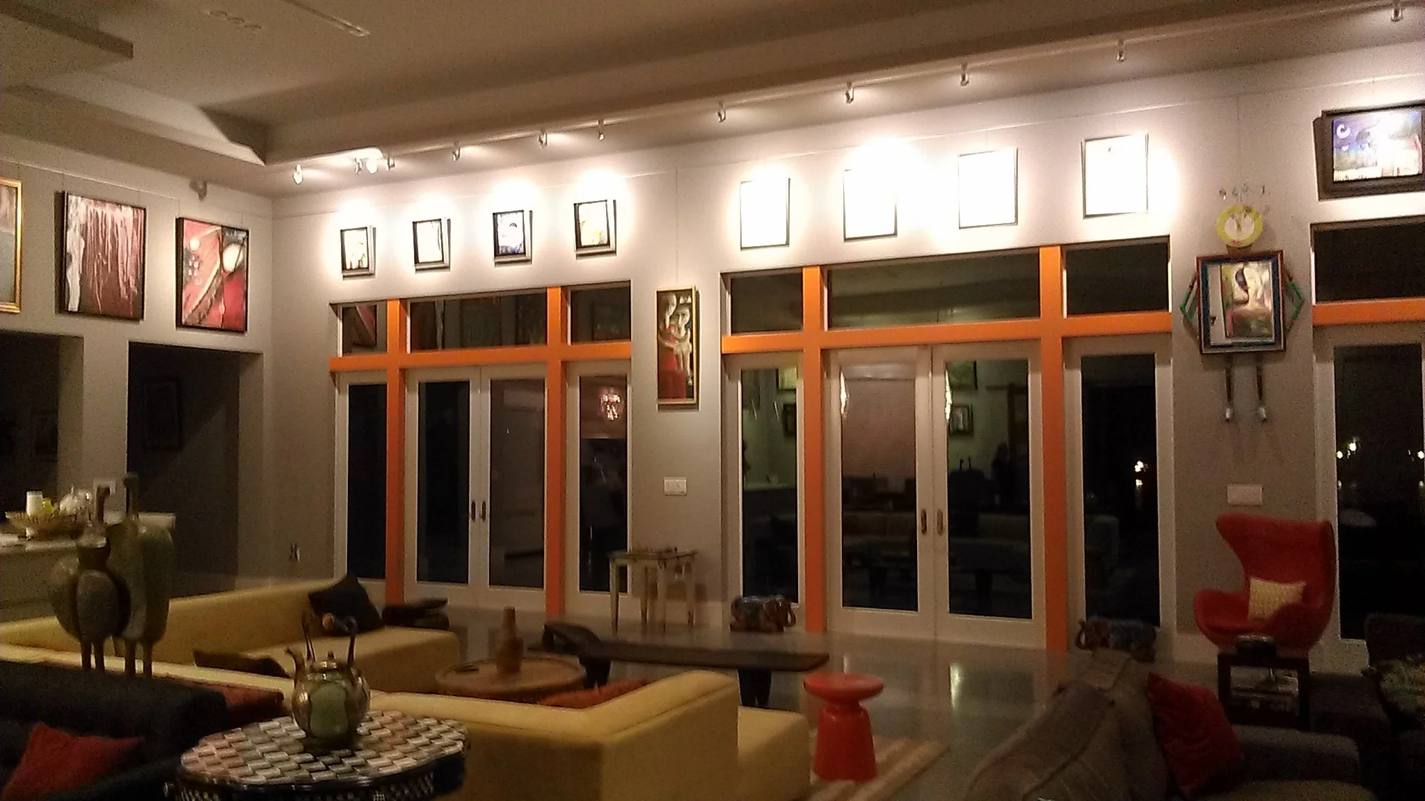 Living room with modern decor, artwork on the walls, large glass doors, and a variety of chairs and sofas arranged for seating.