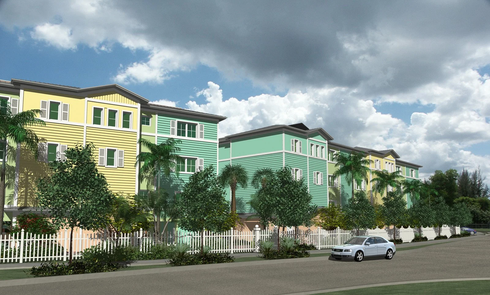 Colorful apartment buildings with yellow and green siding, white trim, palm trees, a white picket fence, and a silver car parked on the street under a partly cloudy sky.