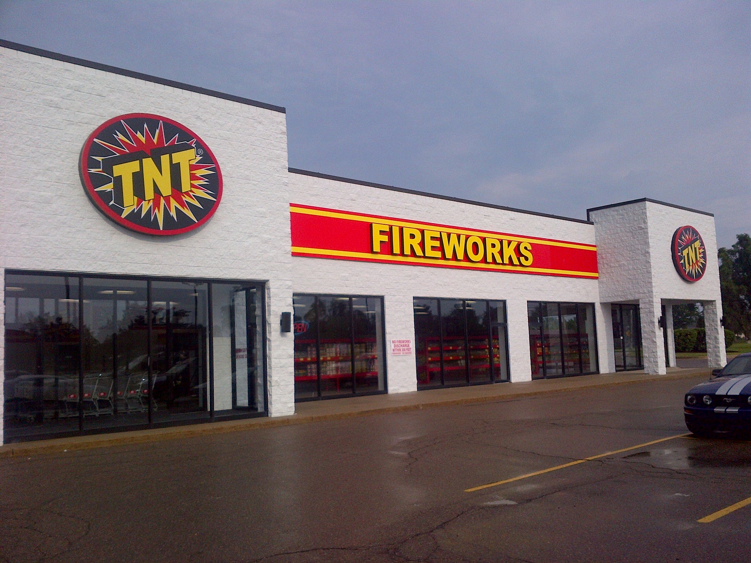 Exterior of TNT Fireworks store with large signs and glass windows, parked cars in front, clear sky