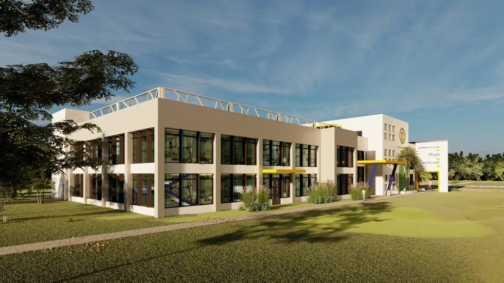 Modern two-story building with large glass windows, surrounded by green grass and trees, under a partly cloudy sky.