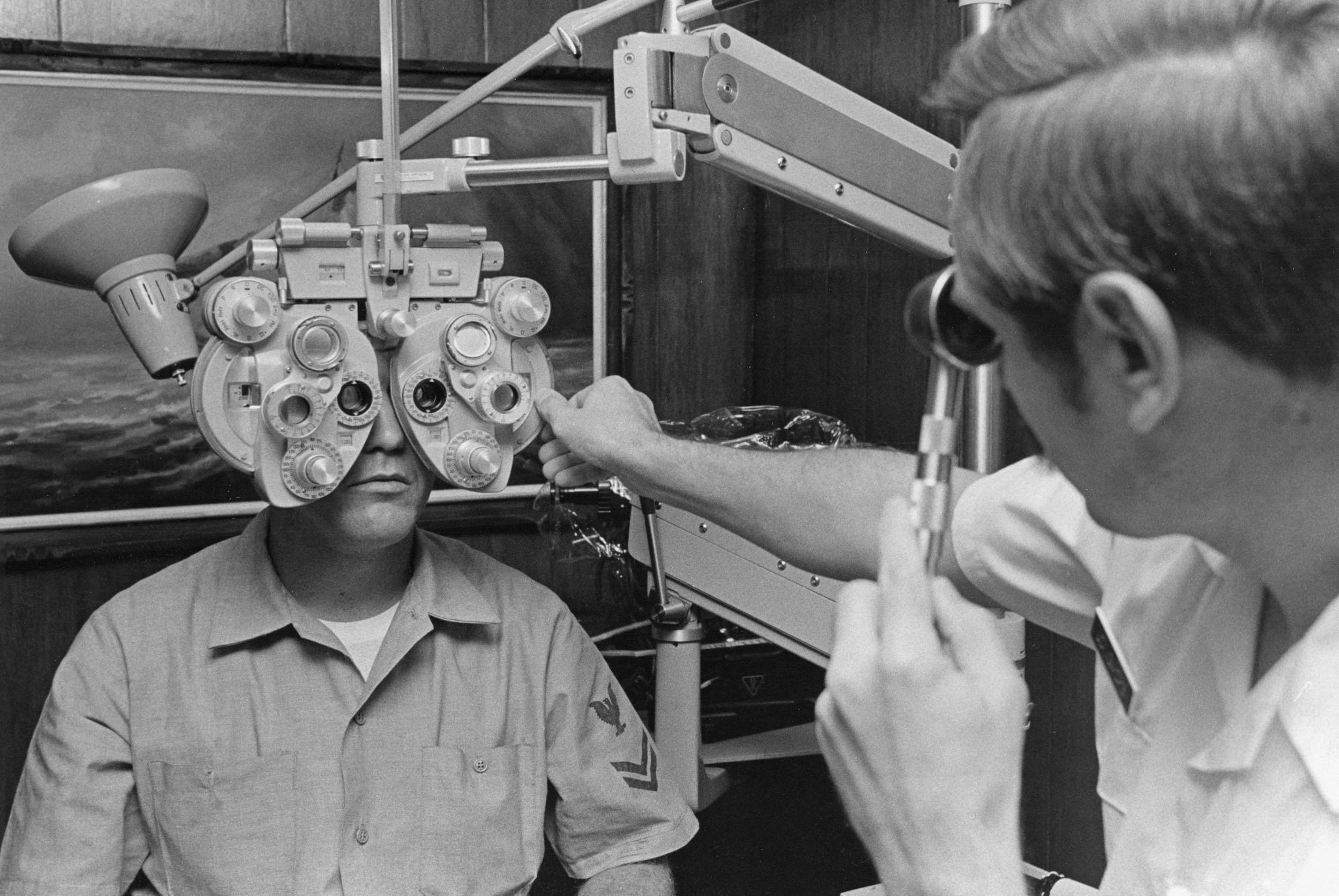 An eye exam where a patient is sitting with a phoropter in front of their face, and an optometrist is adjusting the equipment.