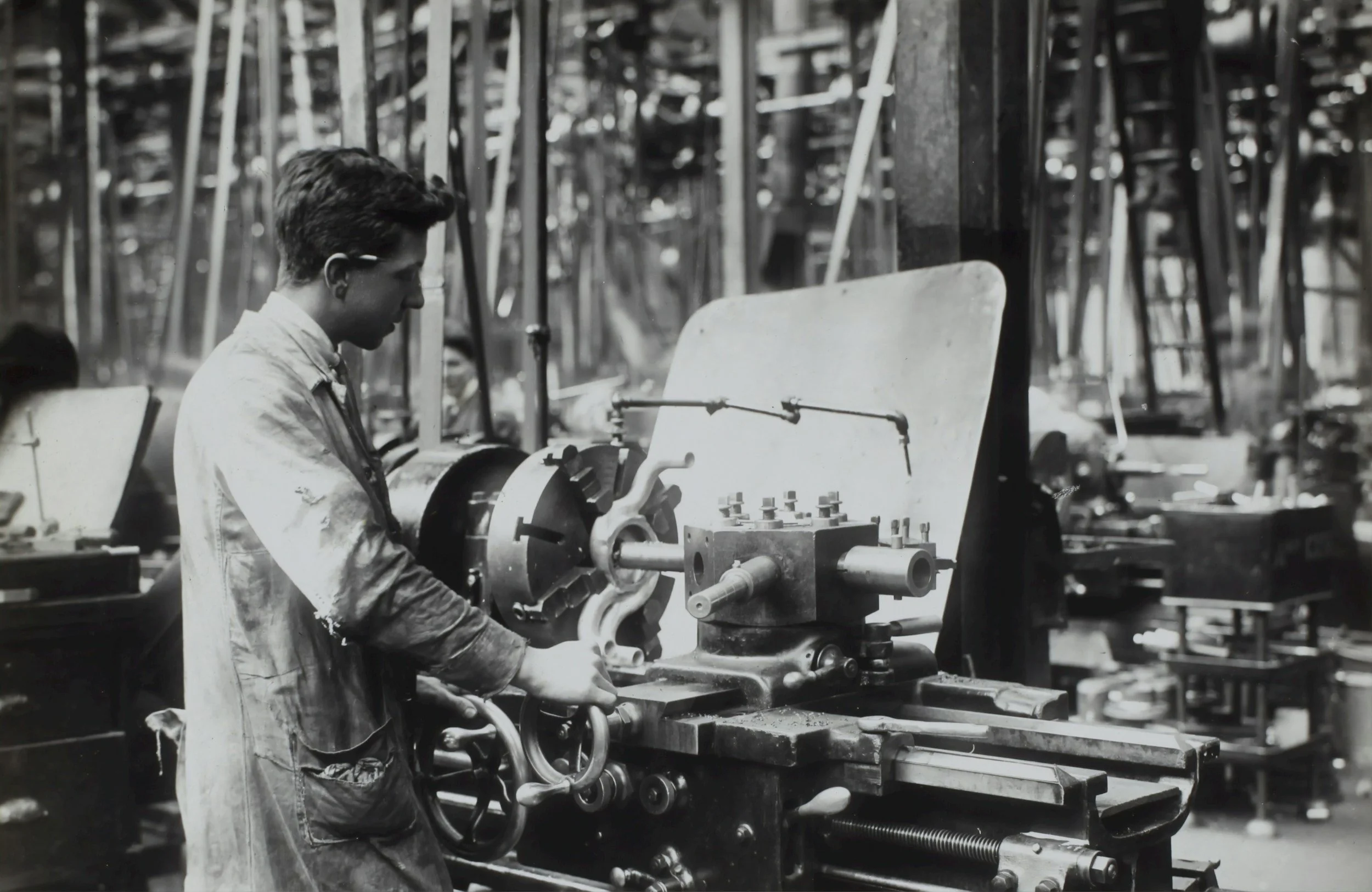 A man working at a machine in an industrial workshop with tools and equipment around.
