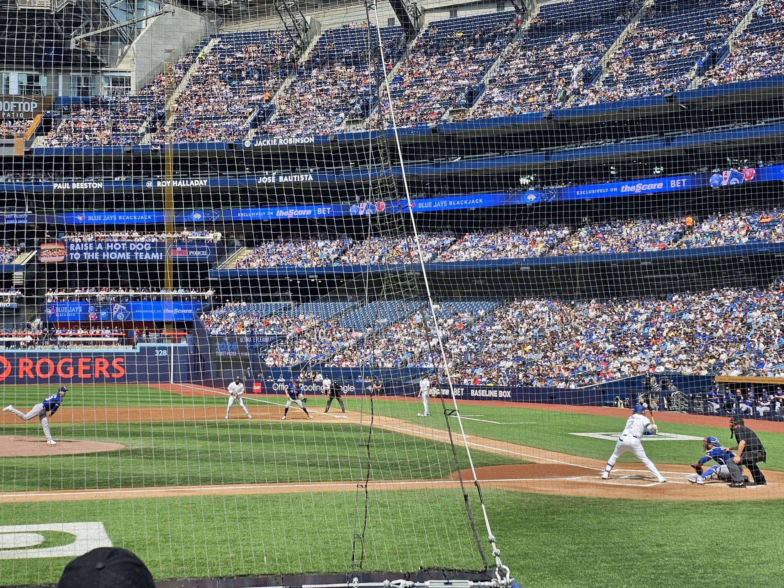 A baseball game in progress at a stadium with a large crowd, players on the field, and advertisements around the outfield walls.