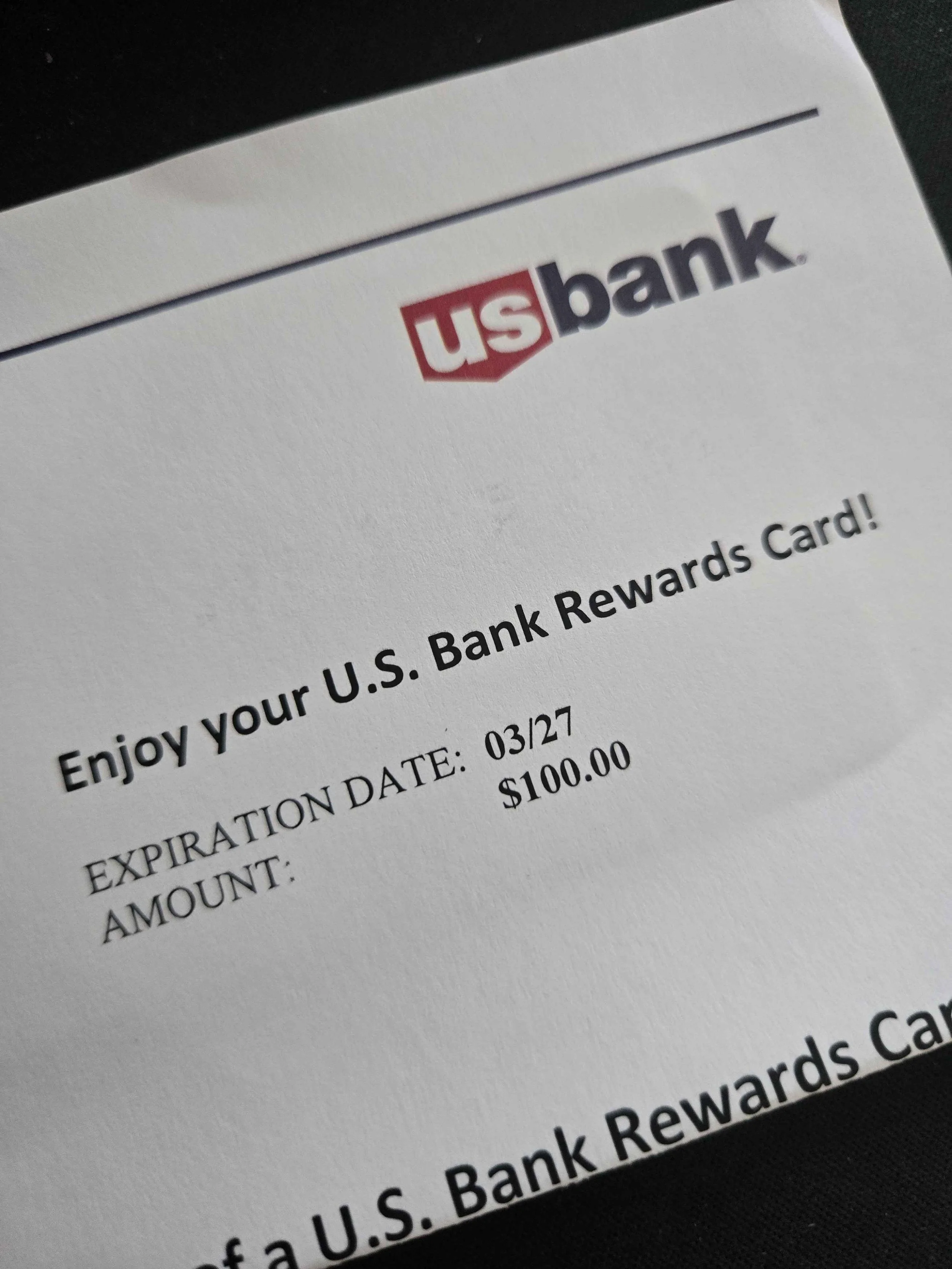 A U.S. Bank rewards card showing an expiration date of 03/27 and an amount of $100.00.