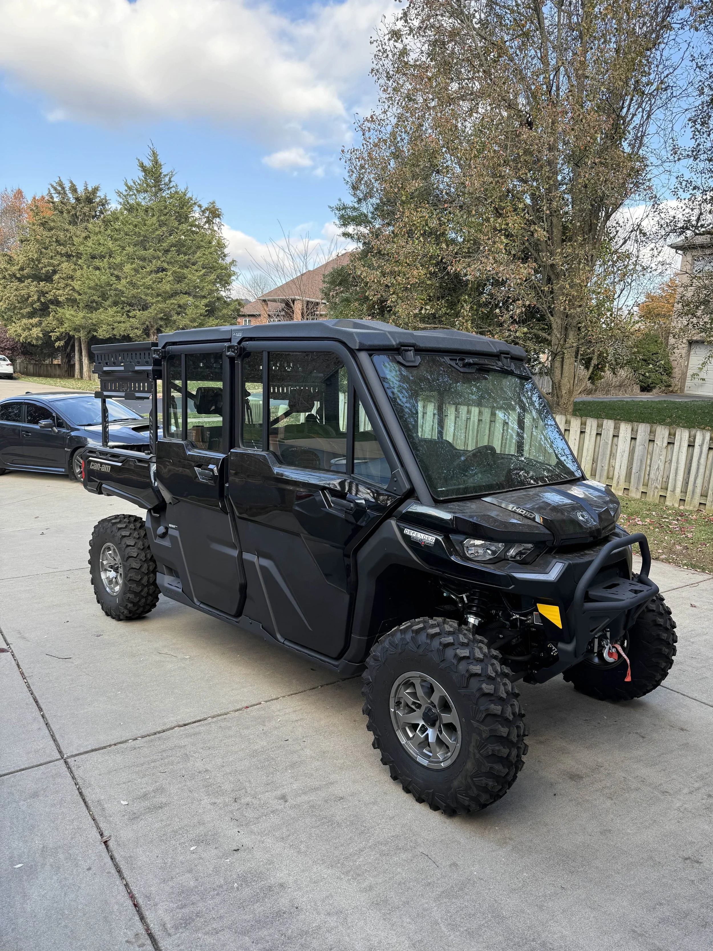 Black all-terrain utility vehicle (UTV) parked on a driveway with trees and houses in the background.